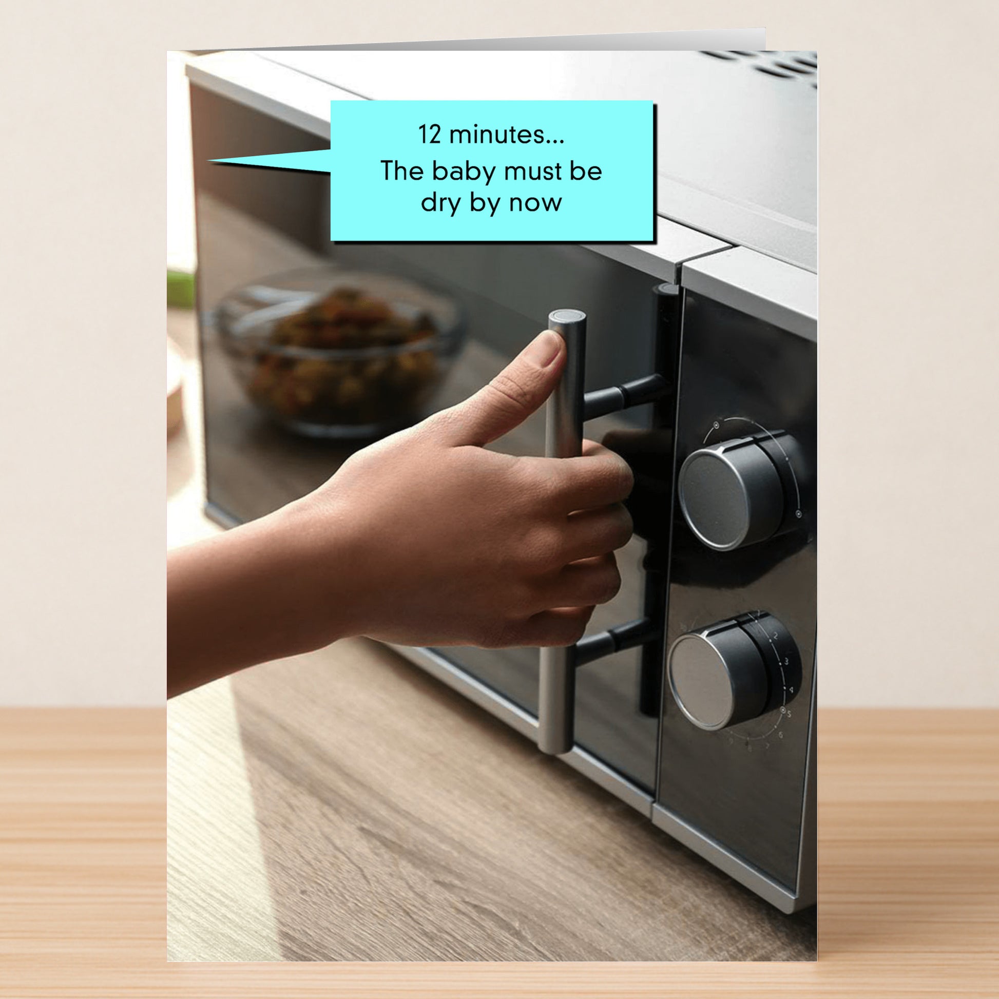The 12 Minutes Funny Greeting Card by Twisted Gifts features a hand opening a microwave door with a speech bubble that says, "12 minutes... The baby must be dry by now," offering a hilarious and unique design sure to make anyone laugh.