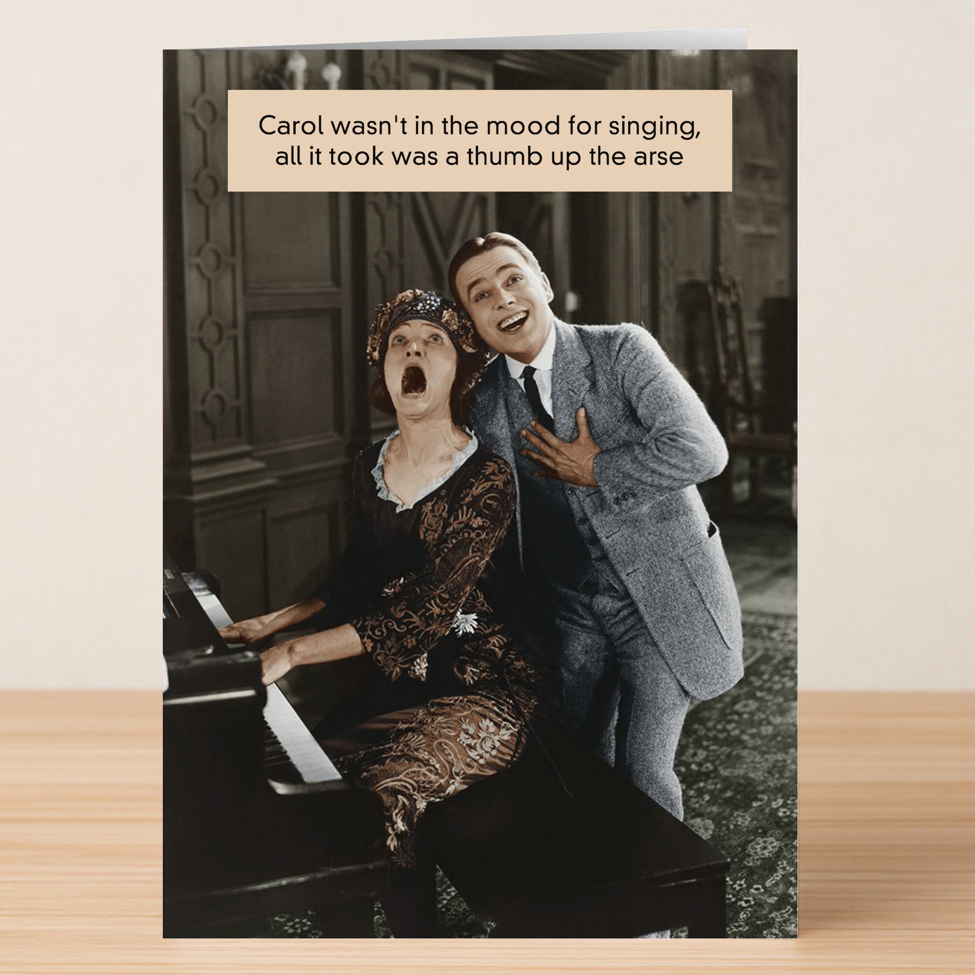 A woman at a piano reacts in surprise as a smiling man stands behind her, hand on chest. Humor text above jokes about her sudden mood shift. The Thumb Rude Greeting Card by Twisted Gifts is perfect for leaving a memorable impression!.