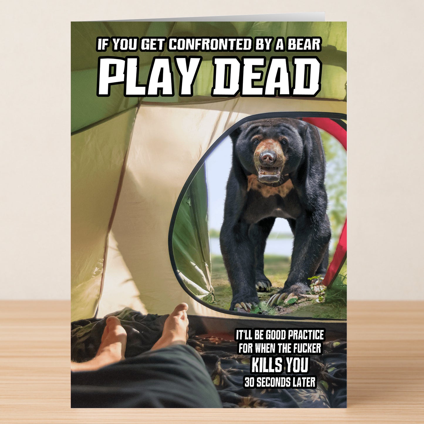 Inside a tent, someone faces an approaching bear; bold text proclaims, "If you get confronted by a bear, play dead," with more darkly witty advice below—just like the Play Dead – Dark Any Occasion Card by Twisted Gifts.