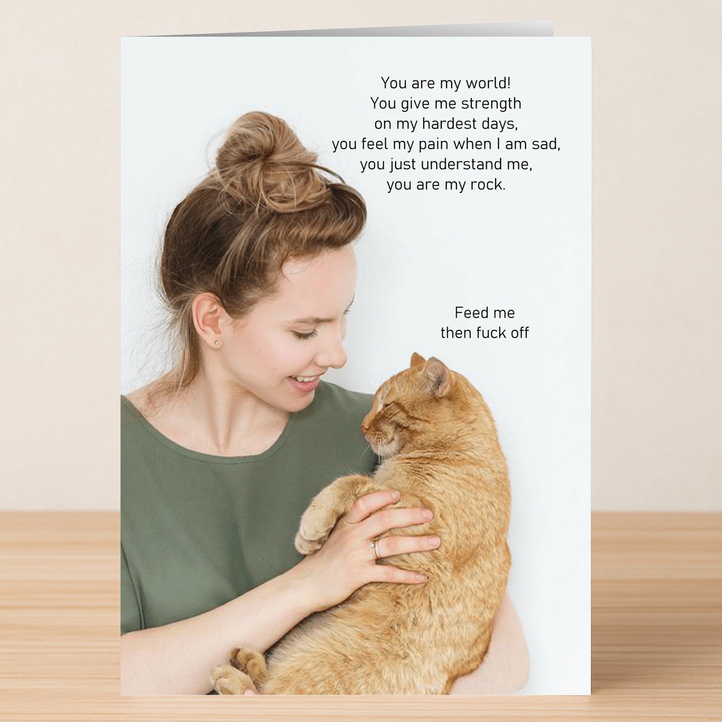 A woman smiles holding an orange cat on the Twisted Gifts Feed Me Funny Greeting Card, which pairs sentimental top text with witty, cat-inspired humor below—perfect for any occasion.