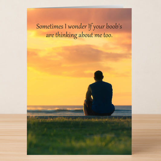 A man sits on grass by the ocean at sunset with text above: "Sometimes I wonder if your boob's are thinking about me too." The "I Wonder" Funny Greeting Card by Twisted Gifts is perfect for those who love witty humor.