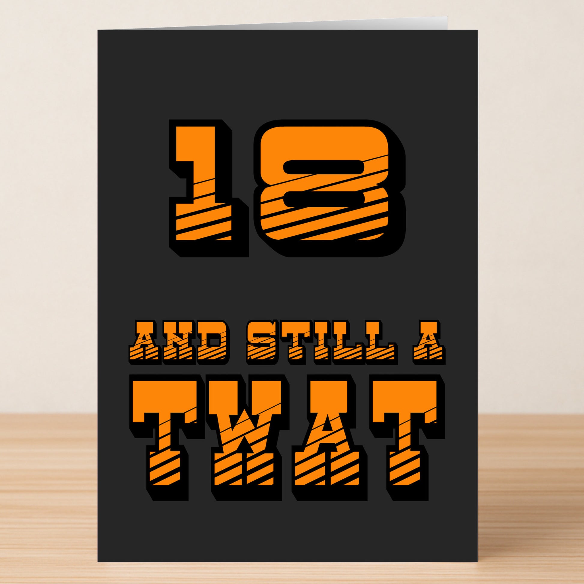 Bold orange text on black reads, "18 - Still A Twat 18 Insulting Birthday Card" by Twisted Gifts—the perfect funny card for anyone who loves a cheeky laugh. Displayed upright on a wooden surface.