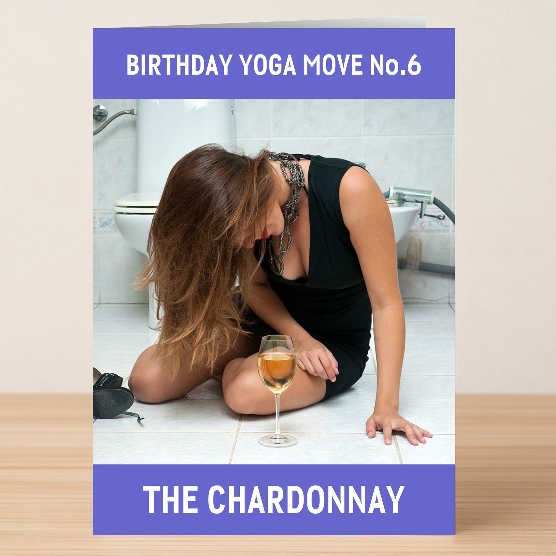 A woman in a black dress kneels on a bathroom floor, head bowed with white wine, beneath "Birthday Yoga Move No.6 - The Chardonnay"—a hilarious design from Twisted Gifts' The Chardonnay Funny Birthday Card.
