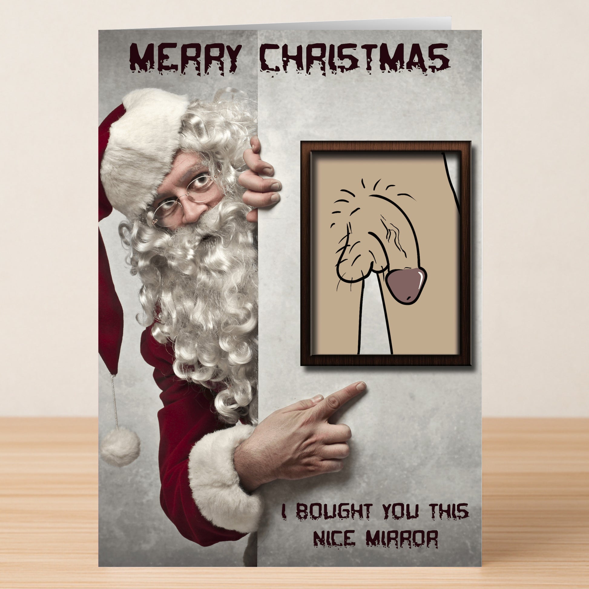 Dressed as Santa, someone points at a framed drawing resembling male genitalia with "Merry Christmas" and "I bought you this nice Mirror Rude Christmas Card," featuring the cheeky Mirror Rude Christmas Card by Twisted Gifts.