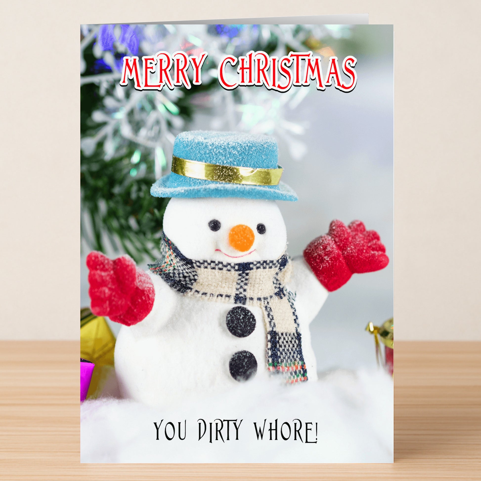 The Dirty Whore Rude Christmas Card by Twisted Gifts features a snowman with scarf, hat, and red gloves raised. "Merry Christmas" headlines the card, while "You dirty whore!" at the bottom adds a cheeky twist.