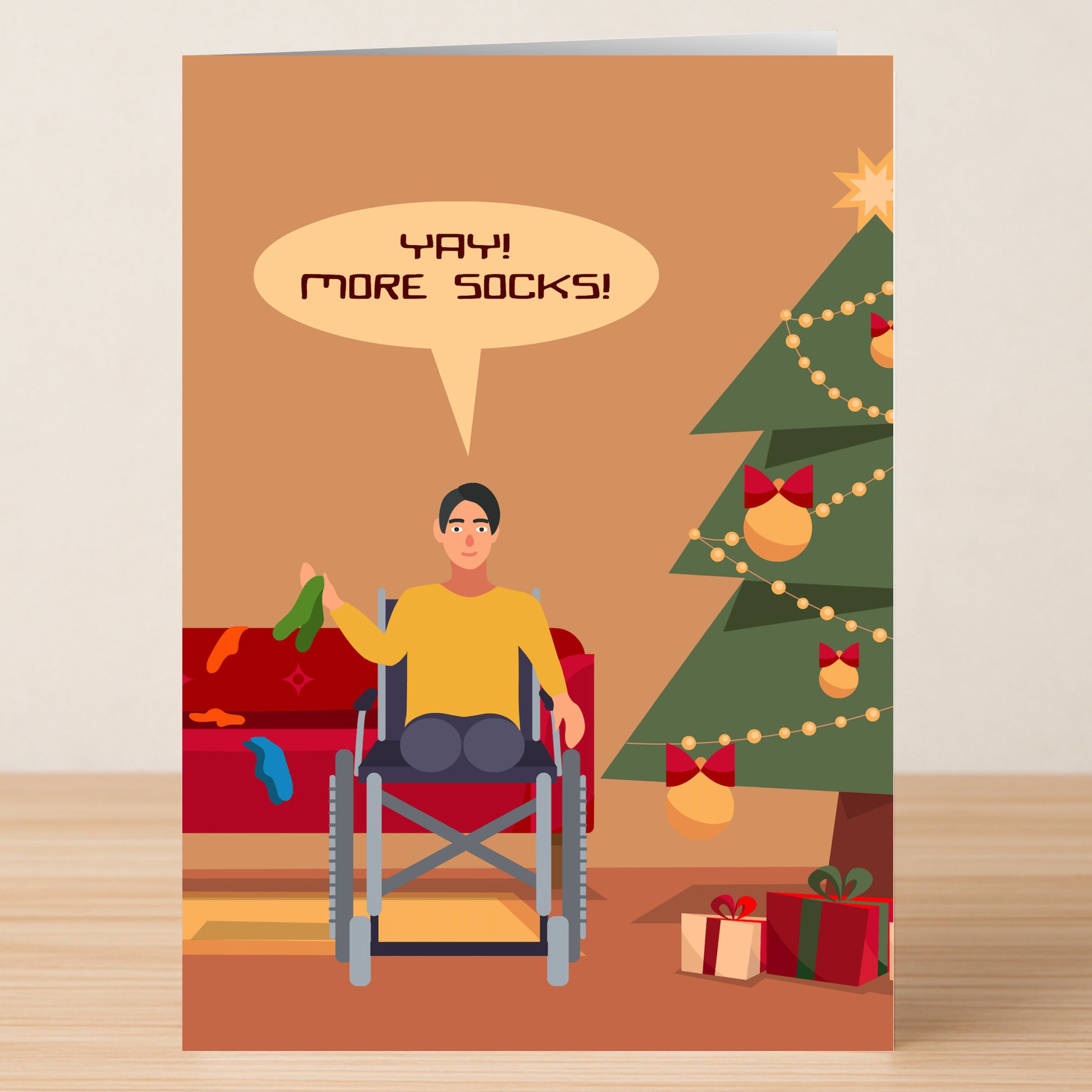 A person in a wheelchair joyfully holds socks by the Christmas tree—perfect for the Twisted Gifts "More Socks Funny Christmas Card" to spread holiday cheer!.