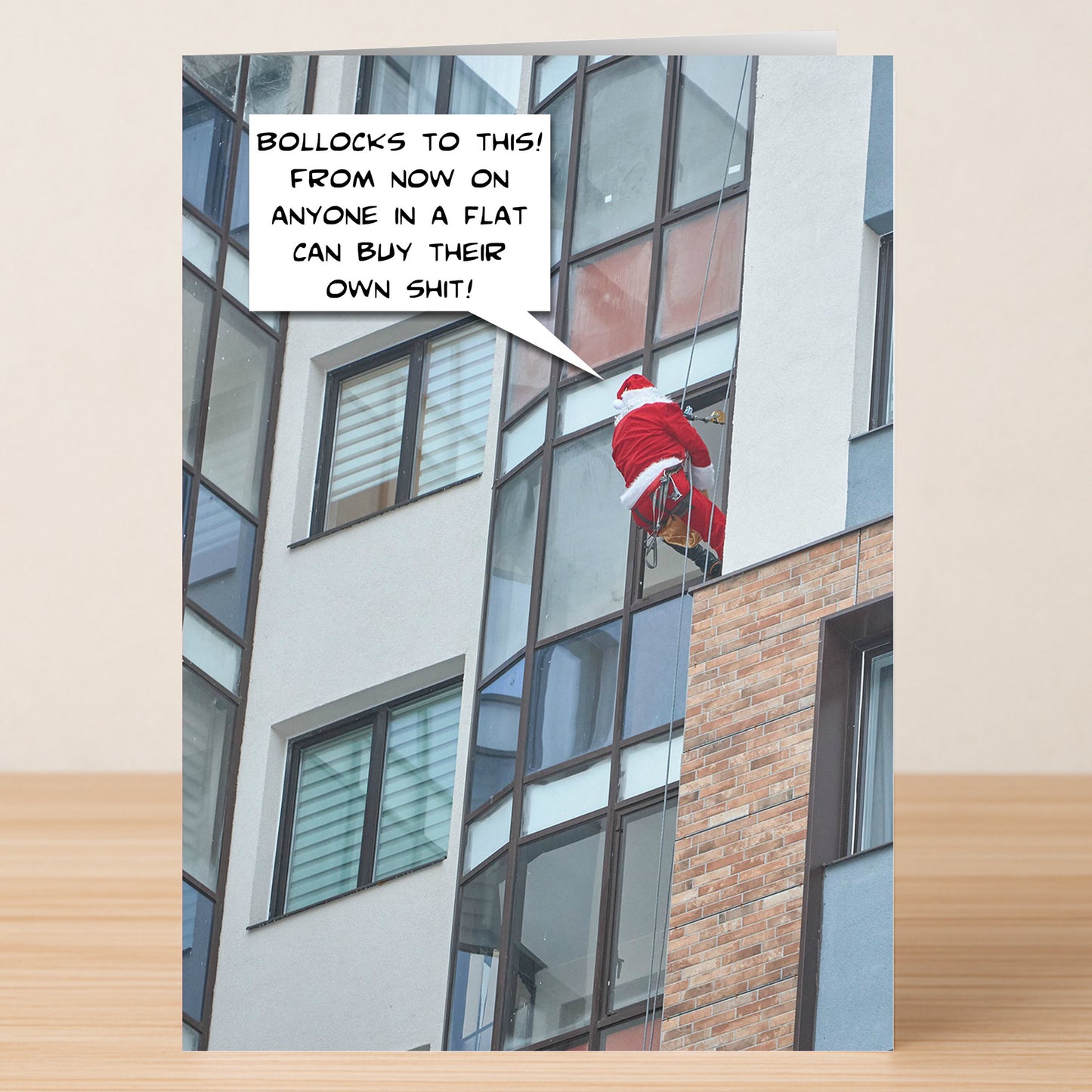 The Flats Funny Christmas Card by Twisted Gifts features Santa abseiling down a modern apartment, humorously complaining about delivering presents to flats—ideal for spreading holiday cheer with a smile.