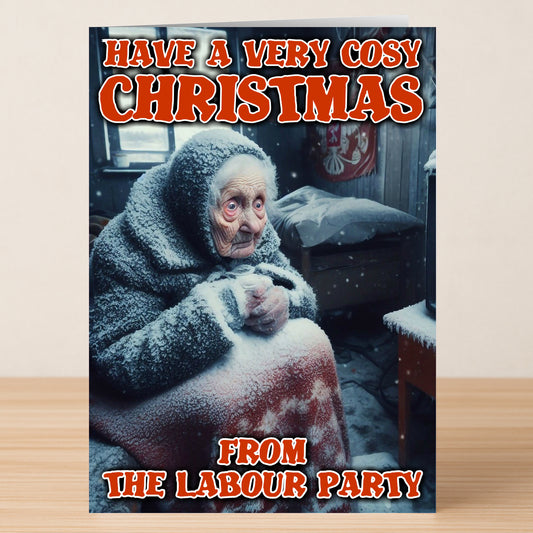 An elderly woman in a snowy room sits wrapped in a blanket. Bold text says, "Have a very cosy Christmas from the Labour Party." The Cosy Funny Christmas Card by Twisted Gifts brings festive humor and warmth.