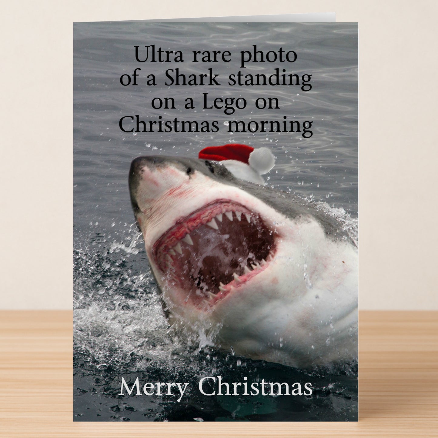 The Lego Shark Funny Christmas Card by Twisted Gifts features a hilarious shark in a Santa hat and playful holiday humor about stepping on Legos. "Merry Christmas" appears at the bottom, making it perfect for festive laughs.