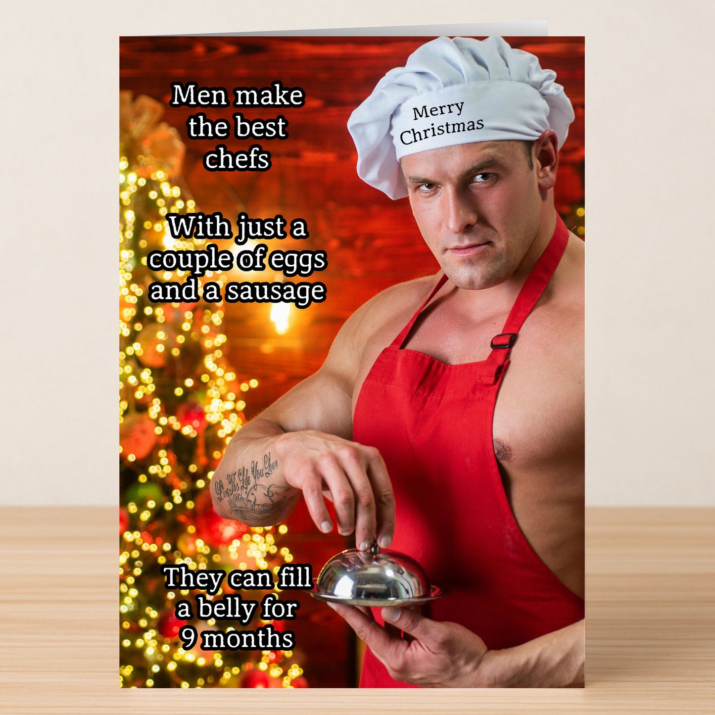 The Best Chef Funny Christmas Card by Twisted Gifts features a muscular man in a chef hat and red apron by a Christmas tree, with the text: "Men make the best chefs... They can fill a belly for 9 months." Ideal holiday humor!.