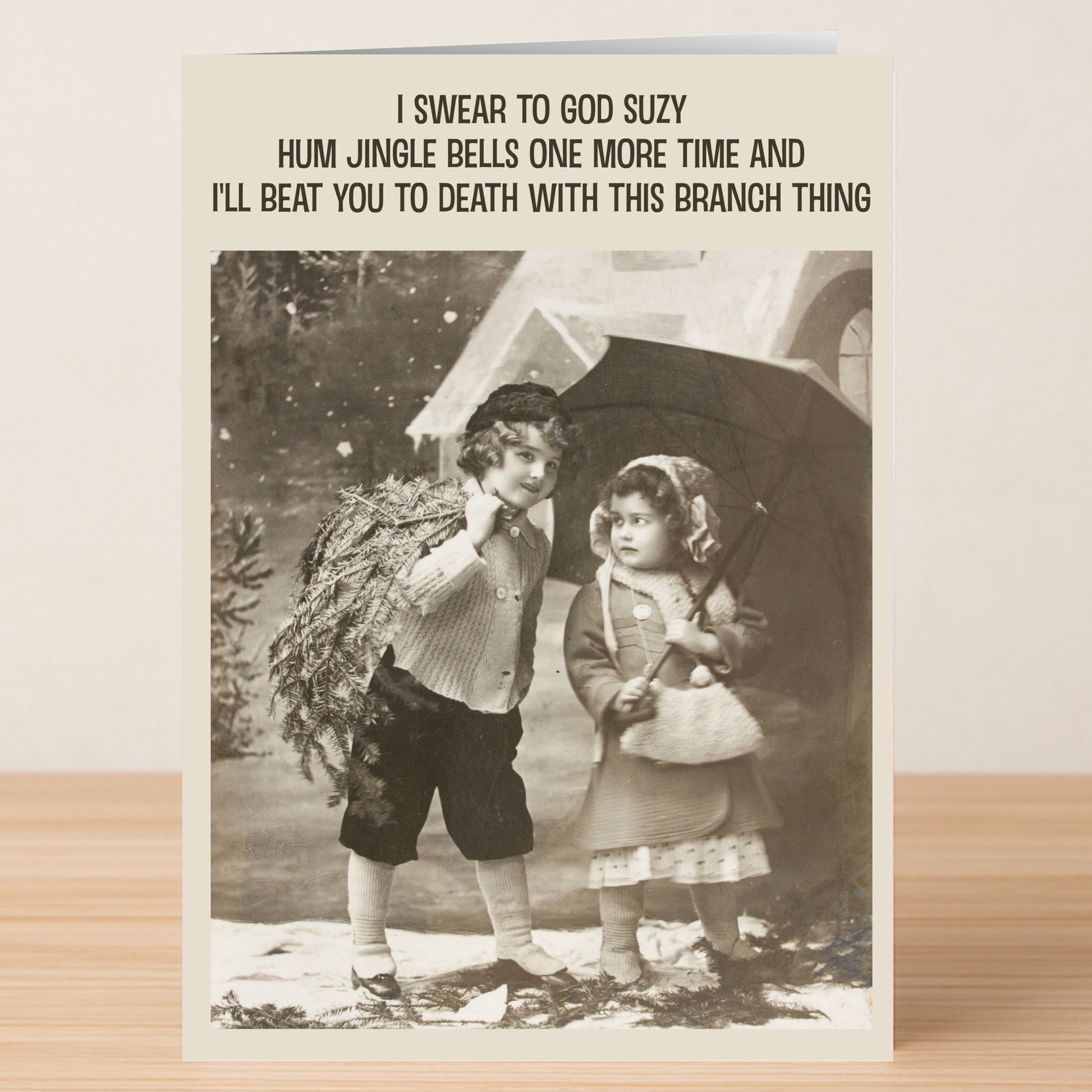 The Jingle Bells, Funny Christmas Card by Twisted Gifts features two kids in winter clothes—one holding an umbrella—with tongue-in-cheek text about threatening to beat someone with a branch.
