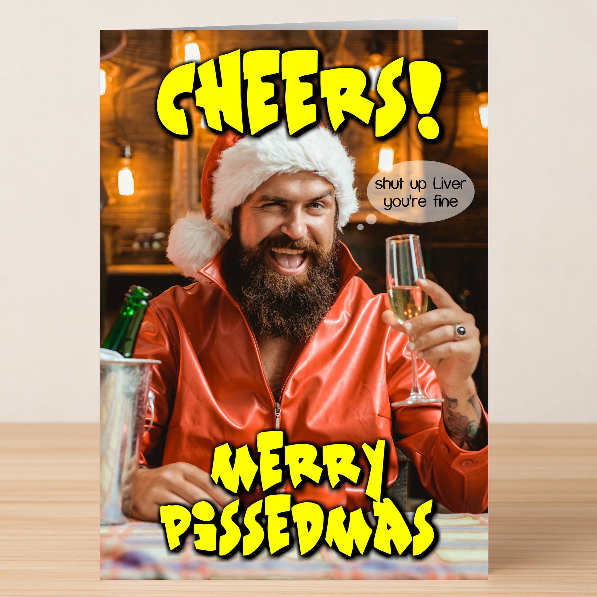 The Shut Up Liver, Funny Christmas Card by Twisted Gifts shows a man in a Santa hat raising a glass with the phrases "CHEERS! Merry Pissedmas" and "shut up Liver you're fine," bringing comic cheer to your holiday celebration.