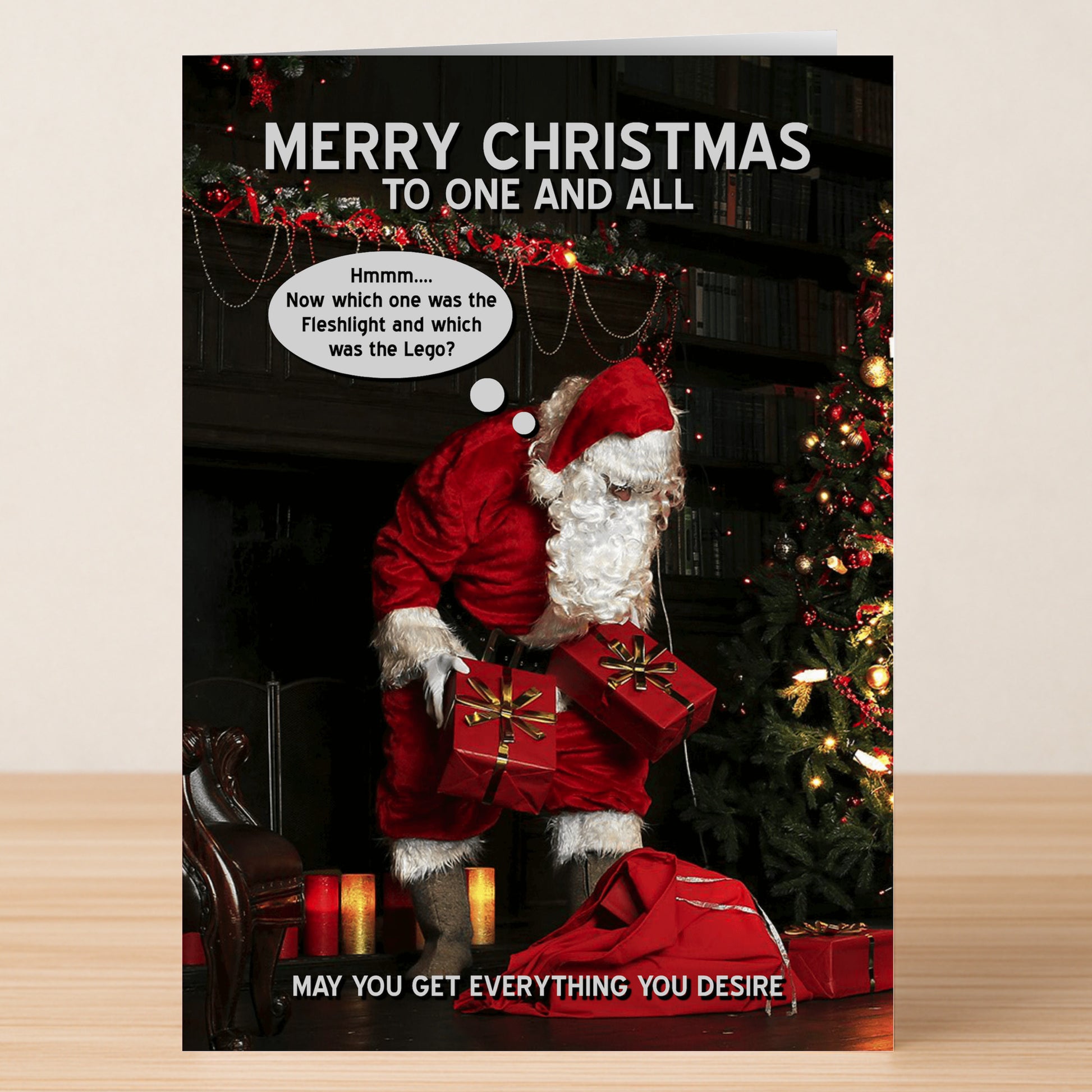 Santa stands by a tree with gifts, thinking, "Hmm... Now which one was the Fleshlight and which was the Lego?" Desire Rude Christmas Card by Twisted Gifts. Features a funny Merry Christmas message and cheeky design.