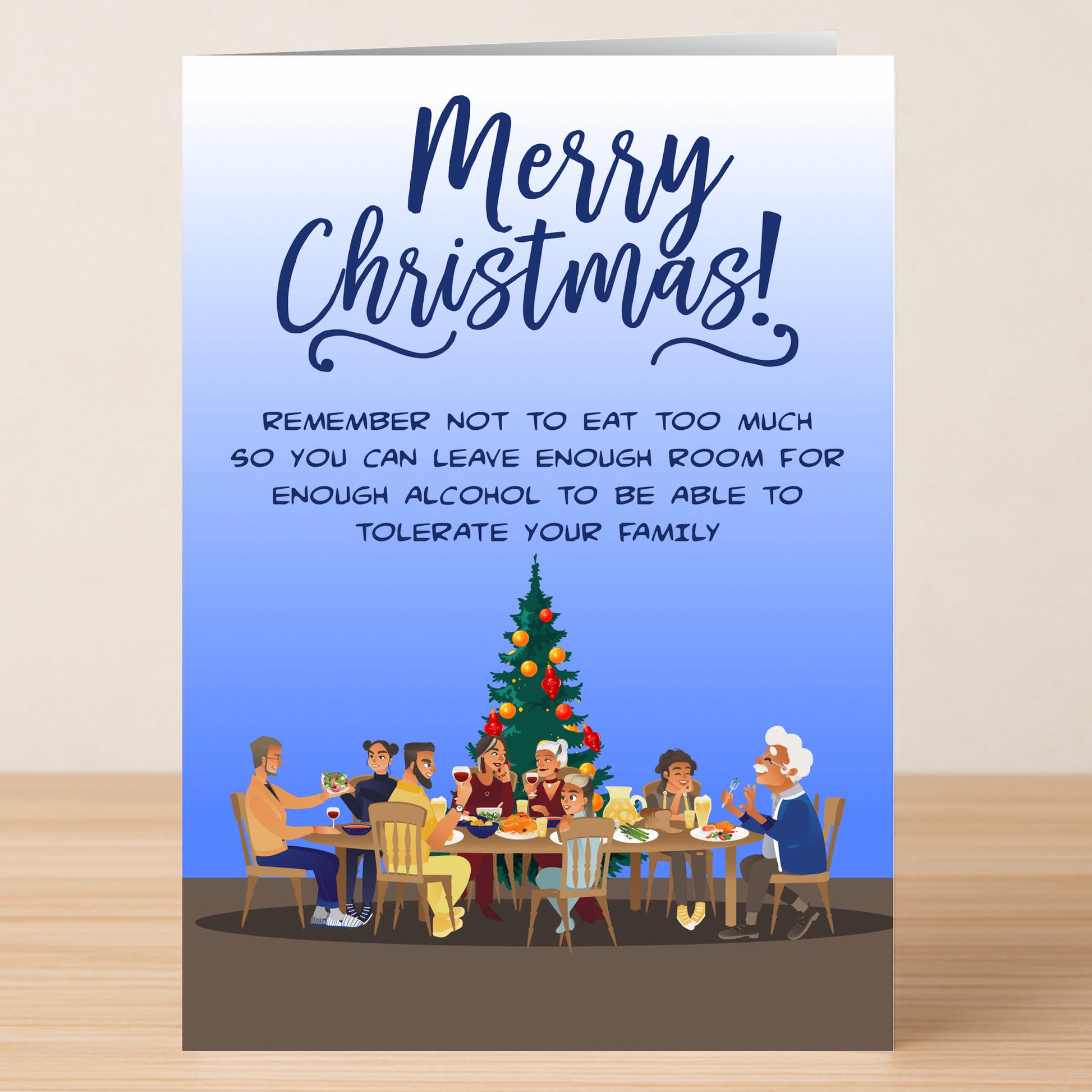 A group sits around a Christmas table under a tree with the message: "Merry Christmas! Twisted Gifts' Tolerate Xmas Funny Christmas Card warns—don’t eat too much; save room for enough alcohol to tolerate your family.