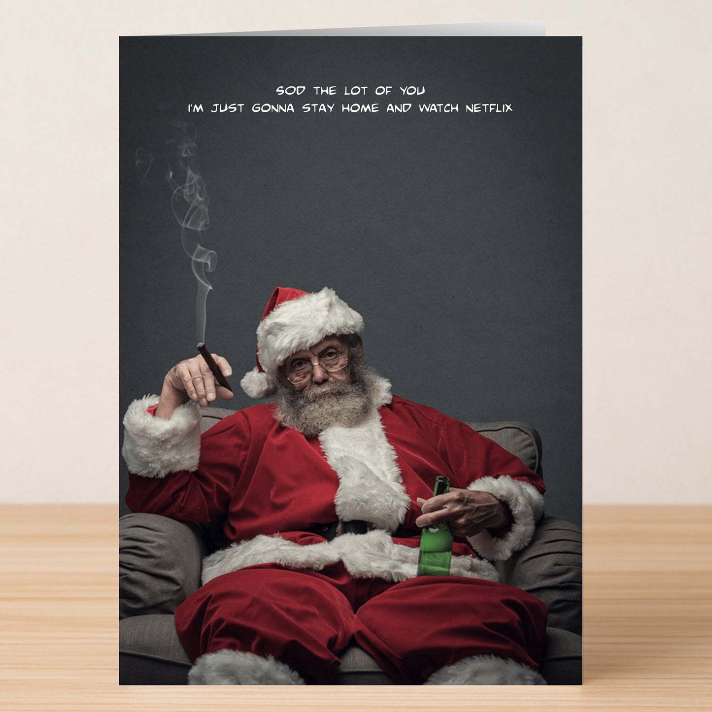 An older man in a Santa suit sits in an armchair, holding a beer and cigarette, with the text: "Sod the lot of you I'm just gonna stay home and watch Netflix." The Netflix Funny Christmas Card by Twisted Gifts brings unexpected holiday humor.
