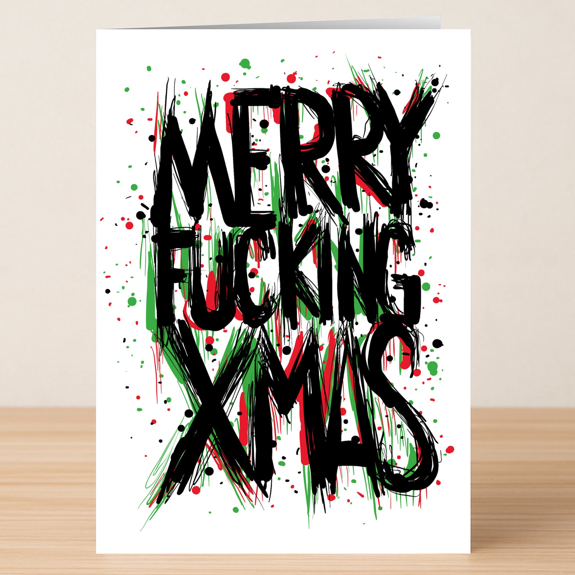 The MFX Funny Christmas Card by Twisted Gifts features bold, jagged “Merry Fucking Xmas” text in black, red, and green with splattered paint on white—a hilarious way to spread holiday cheer and make your loved ones laugh.