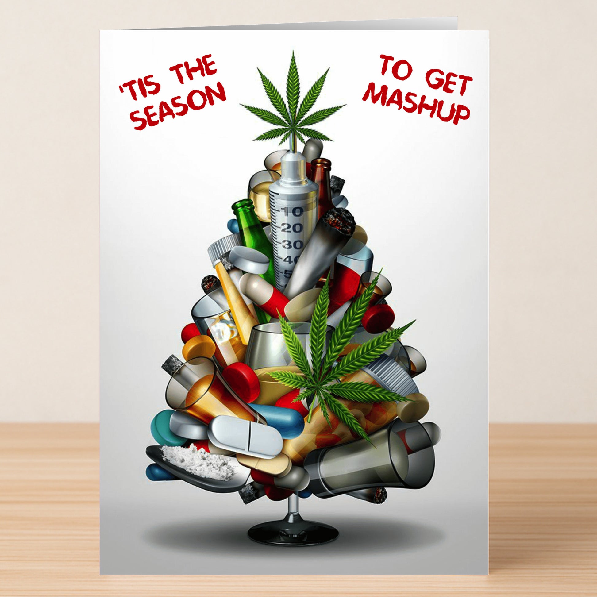 The Mashup Funny Christmas Card by Twisted Gifts features a Christmas tree made of drugs and syringes, decorated with cannabis leaves. The card reads "'Tis the season to get mashup," bringing quirky holiday cheer.