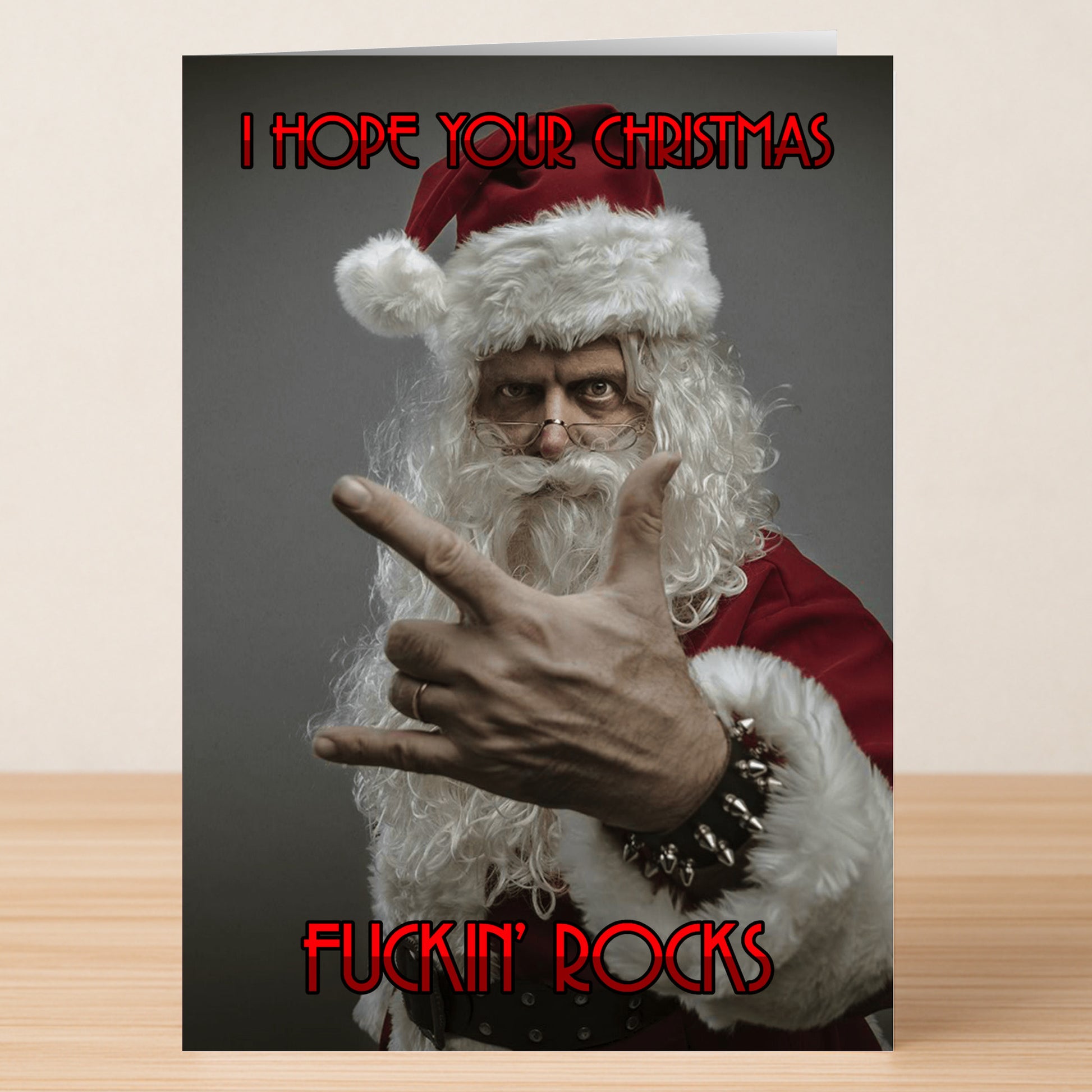 The Xmas Rocks Funny Christmas Card by Twisted Gifts features a Santa making a rock hand gesture with the message "I HOPE YOUR CHRISTMAS FUCKIN' ROCKS" in bold red text, perfect for spreading festive cheer to those who love Xmas with attitude!.
