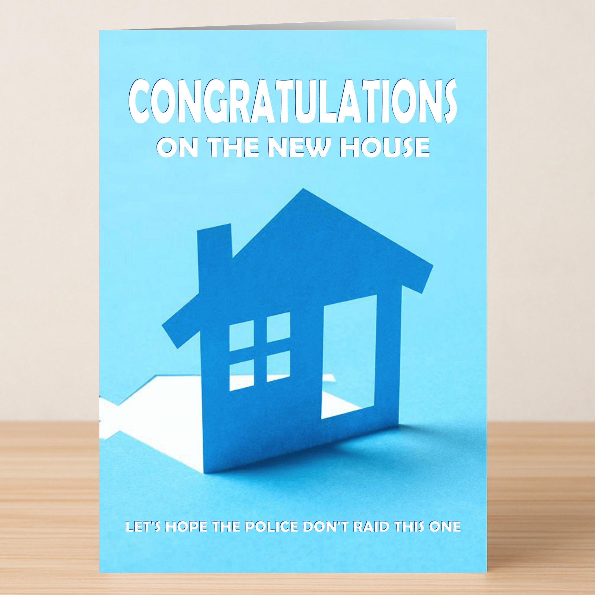 Twisted Gifts' Raid Funny Congratulations Card features a blue paper house cutout with the message: "Congratulations on the new house. Let's hope the police don't raid this one," printed in crisp white text.