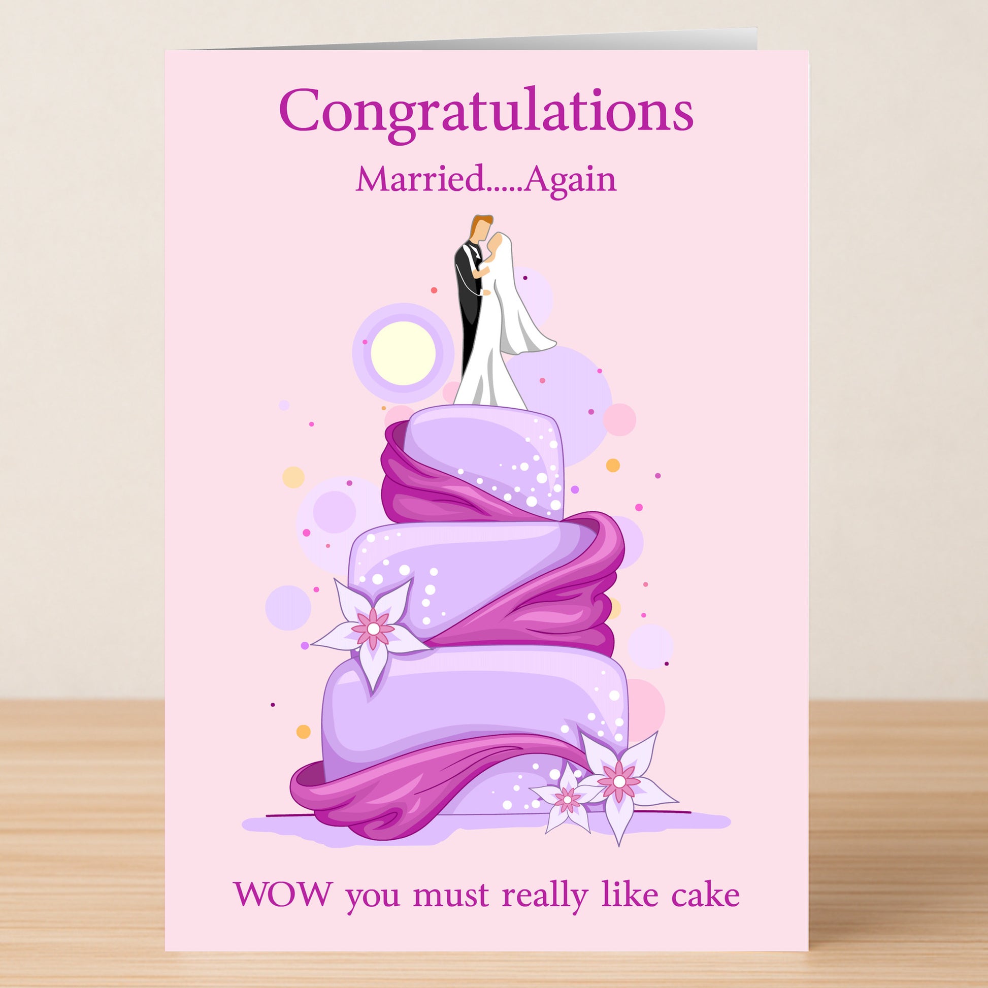 The Married Again Insulting Congratulations Card by Twisted Gifts features a cartoon couple on a purple wedding cake with the text: "Congratulations Married...Again WOW you must really like cake." Perfect for second weddings and those who love humor!.