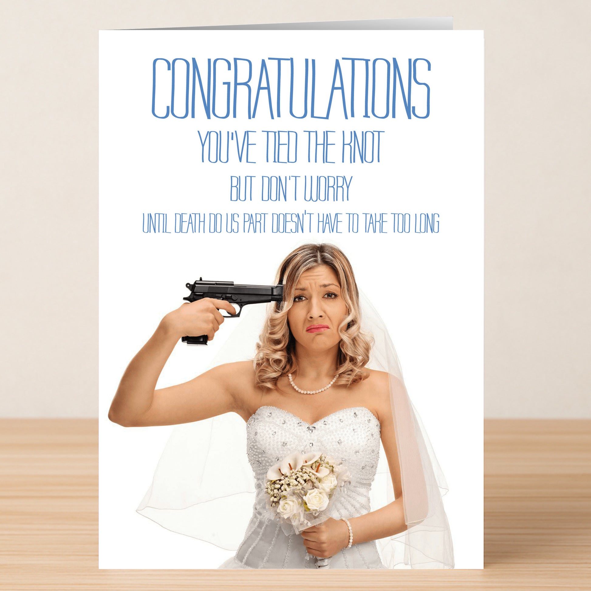 A bride in a wedding dress points a pistol at her head, looking unhappy. The Twisted Gifts Death Do Us Part Funny Congratulations Card delivers dark humor: “Congratulations, you’ve tied the knot… but ‘til death do us part doesn’t have to take too long.”.