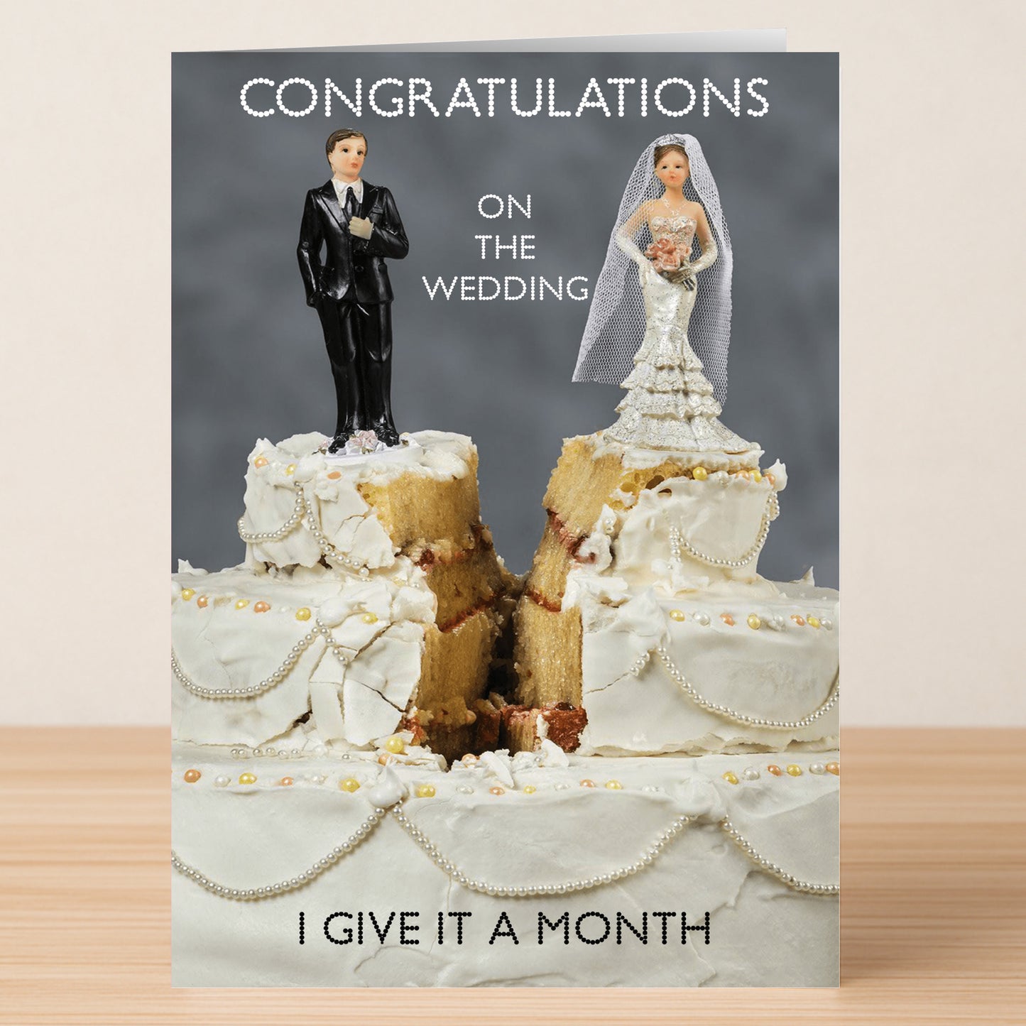 The "A Month Funny Congratulations Card" by Twisted Gifts features bride and groom figurines on a split wedding cake with the message: "Congratulations on the wedding. I give it a month.