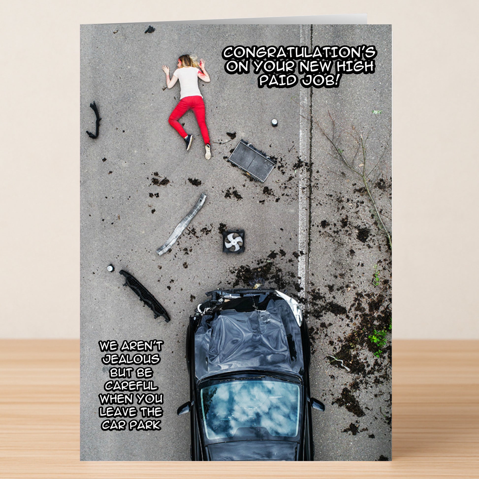 The High Paid Job Funny Congratulations Card by Twisted Gifts features an aerial view of a crashed car, debris, and a person on the ground, paired with sarcastic text about landing a high-paying job and being careful in the car park.