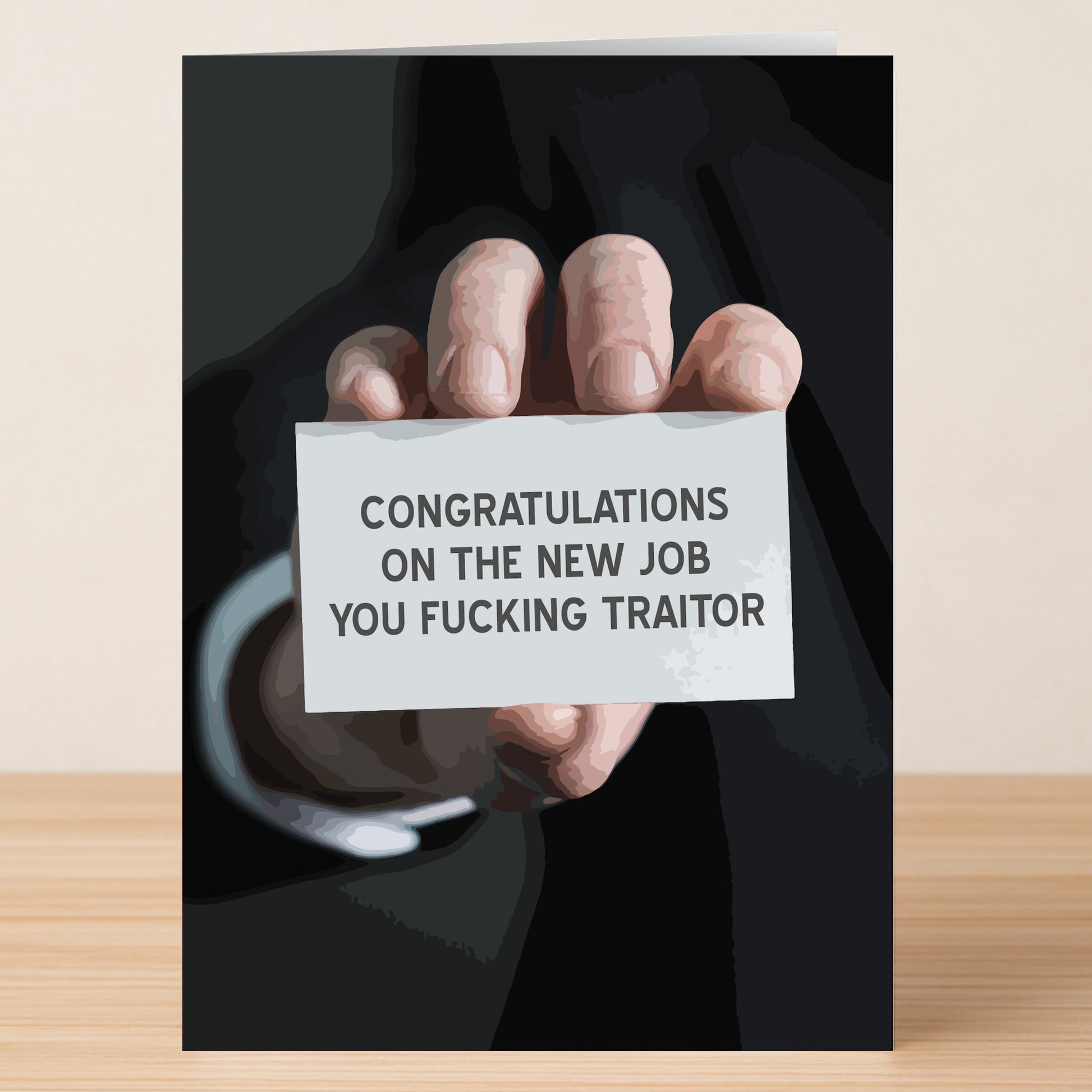 A hand in a black suit holds the Twisted Gifts Traitor Insulting Congratulations Card, featuring the bold text, "CONGRATULATIONS ON THE NEW JOB YOU FUCKING TRAITOR"—a funny way to celebrate with attitude.