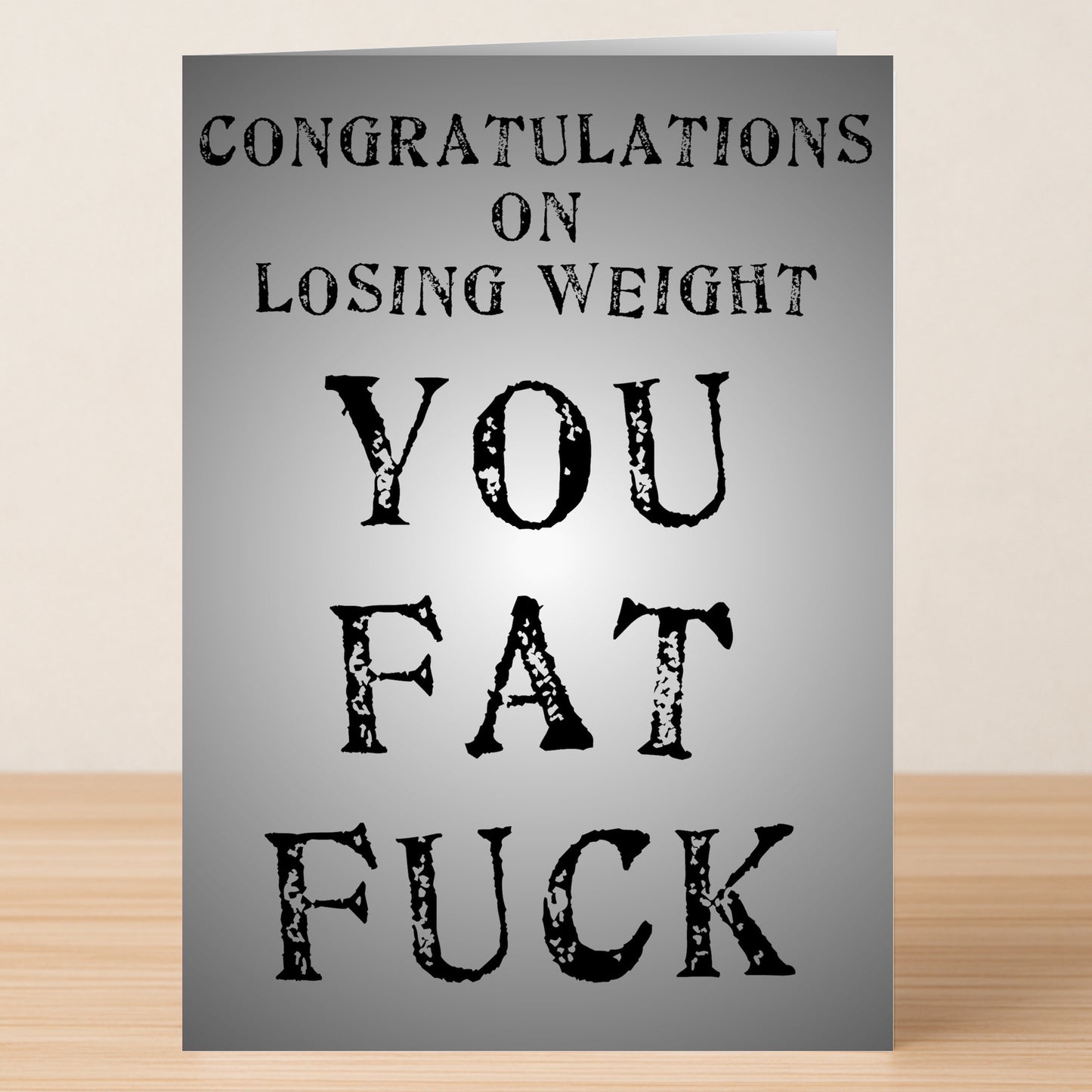 The Losing Weight Insulting Congratulations Card by Twisted Gifts features bold, distressed black text on a gray background with the message: "Congratulations on losing weight. You fat fuck." Perfect for blunt, honest celebrations.