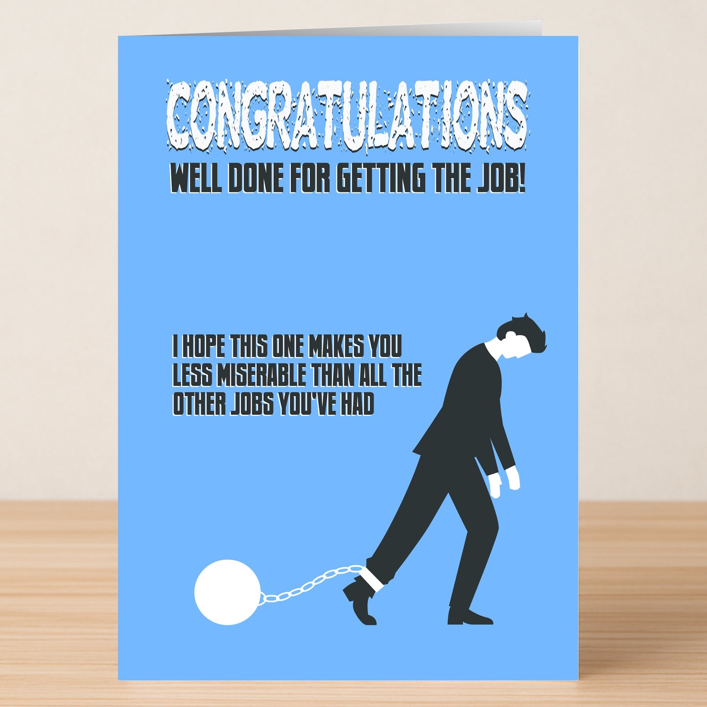 Celebrate a new job with the Miserable Funny Congratulations Card from Twisted Gifts—featuring witty wordplay, a suit-clad figure chained to a ball, and playful text for a quirky twist on workplace congratulations.