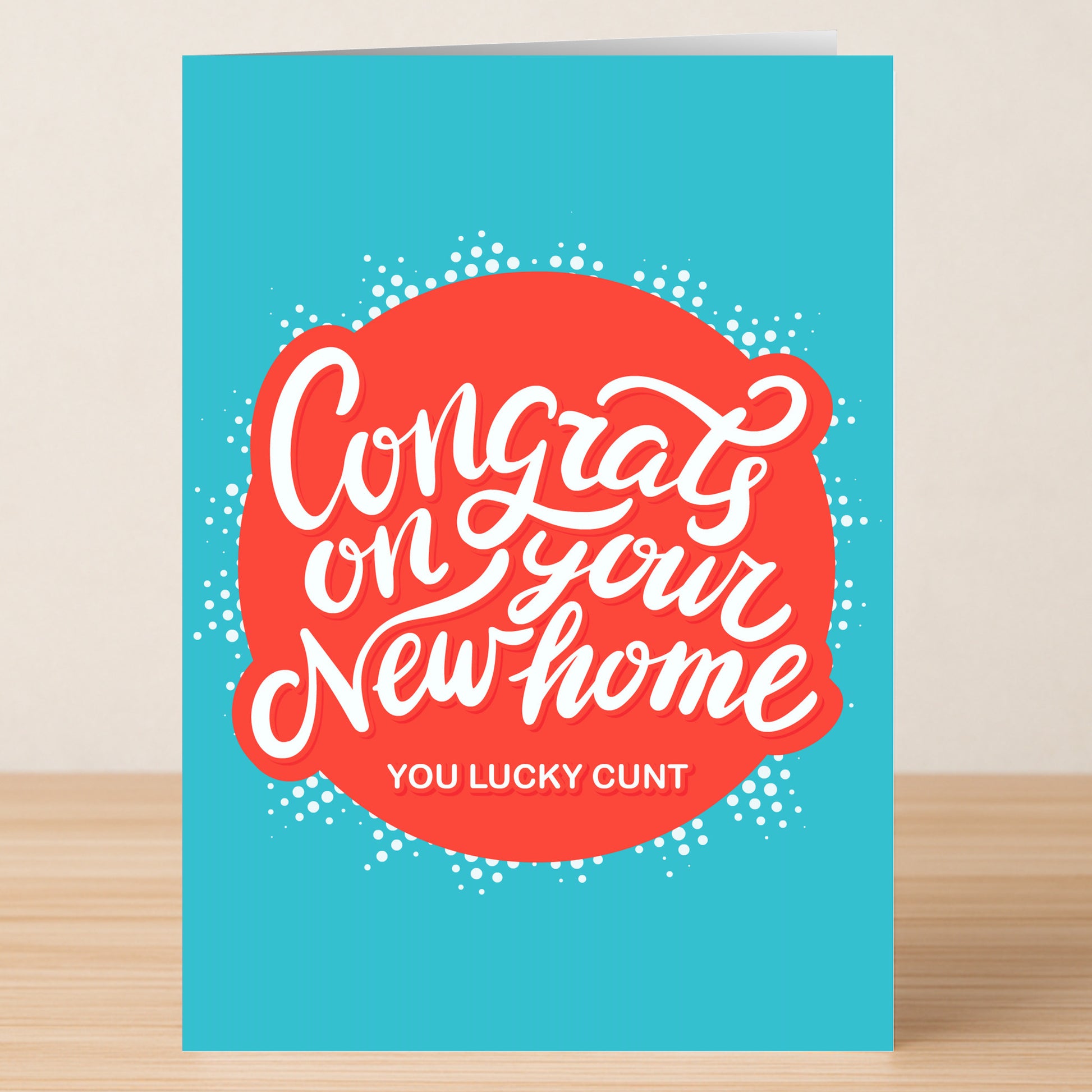 The Lucky Cunt Rude Congratulations Card by Twisted Gifts features a blue background, red circle, and "Congrats on your new home, you lucky cunt" in white script. This bold card is perfect for celebrating with humor.