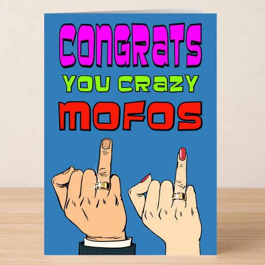 The Mofos Insulting Congratulations Card by Twisted Gifts features bold "Congrats You Crazy Mofos" text, two hands flipping the bird with rings, and a blue background—ideal for friends who love explicit language and cheeky humor.