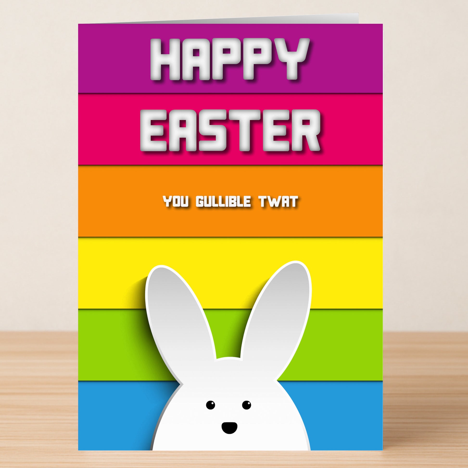 Twisted Gifts’ Gullible Insulting Easter Card features a vibrant rainbow background, cartoon bunny ears, and the text "HAPPY EASTER You gullible twat"—ideal for those who love witty insults and cheeky humor.