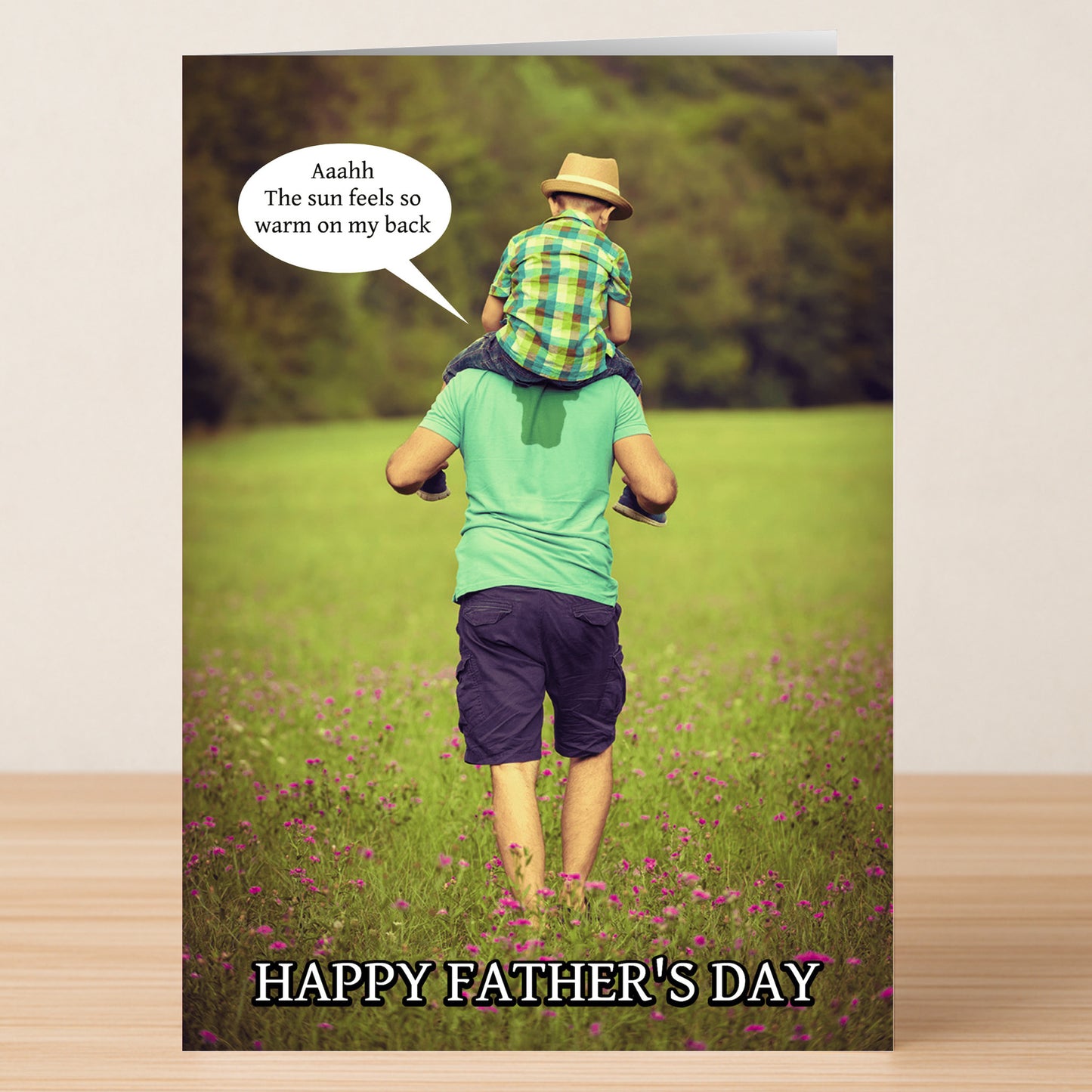 A man carries a child on his shoulders in a field as the child says, "Aaahh, the sun feels so warm on my back." "HAPPY FATHER'S DAY" appears below. Warm Back Funny Father's Day Card by Twisted Gifts—perfect for Father's Day!.