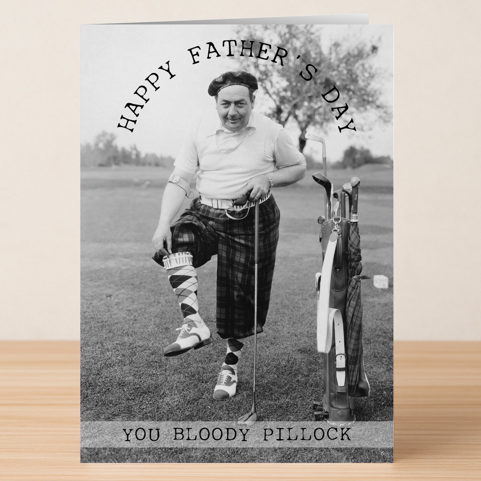 The Twisted Gifts Pillock Insulting Father's Day Card features a man in golfing plaid adjusting his sock by a golf bag with the message "Happy Father's Day. You bloody pillock." Perfect for a unique and funny greeting.