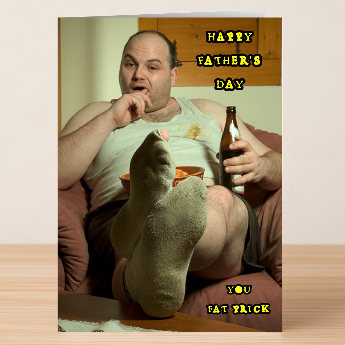 A man in a tank top relaxes with beer and snacks, feet up, as "Happy Father's Day You Fat Prick" appears. The Fat Prick Insulting Father's Day Card by Twisted Gifts is perfect for a hilarious greeting or unique dad gift.