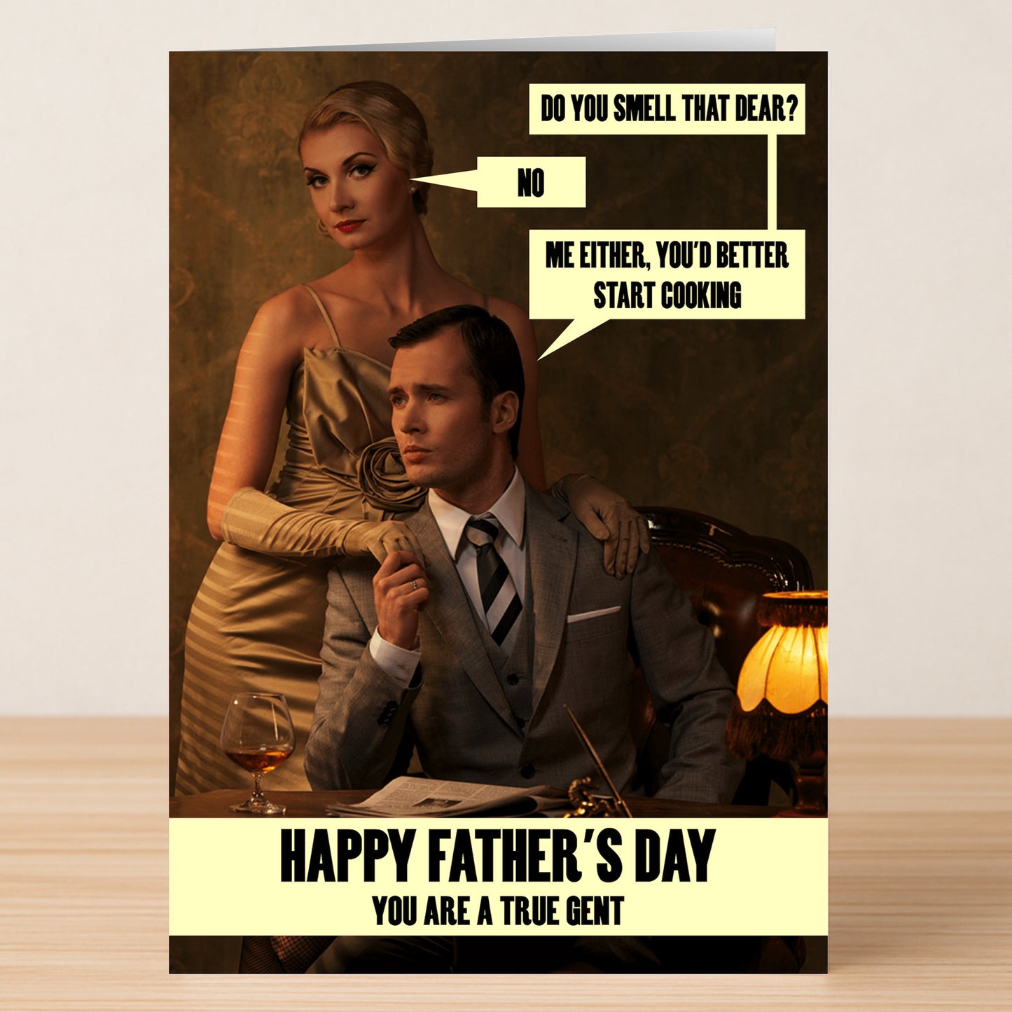 A woman in gold stands behind a seated dad in a suit. Dialogue: "Do you smell that dear?" "No." "Me either, you'd better start cooking." Text: True Gent Funny Father's Day Card by Twisted Gifts—humorous and heartfelt!.