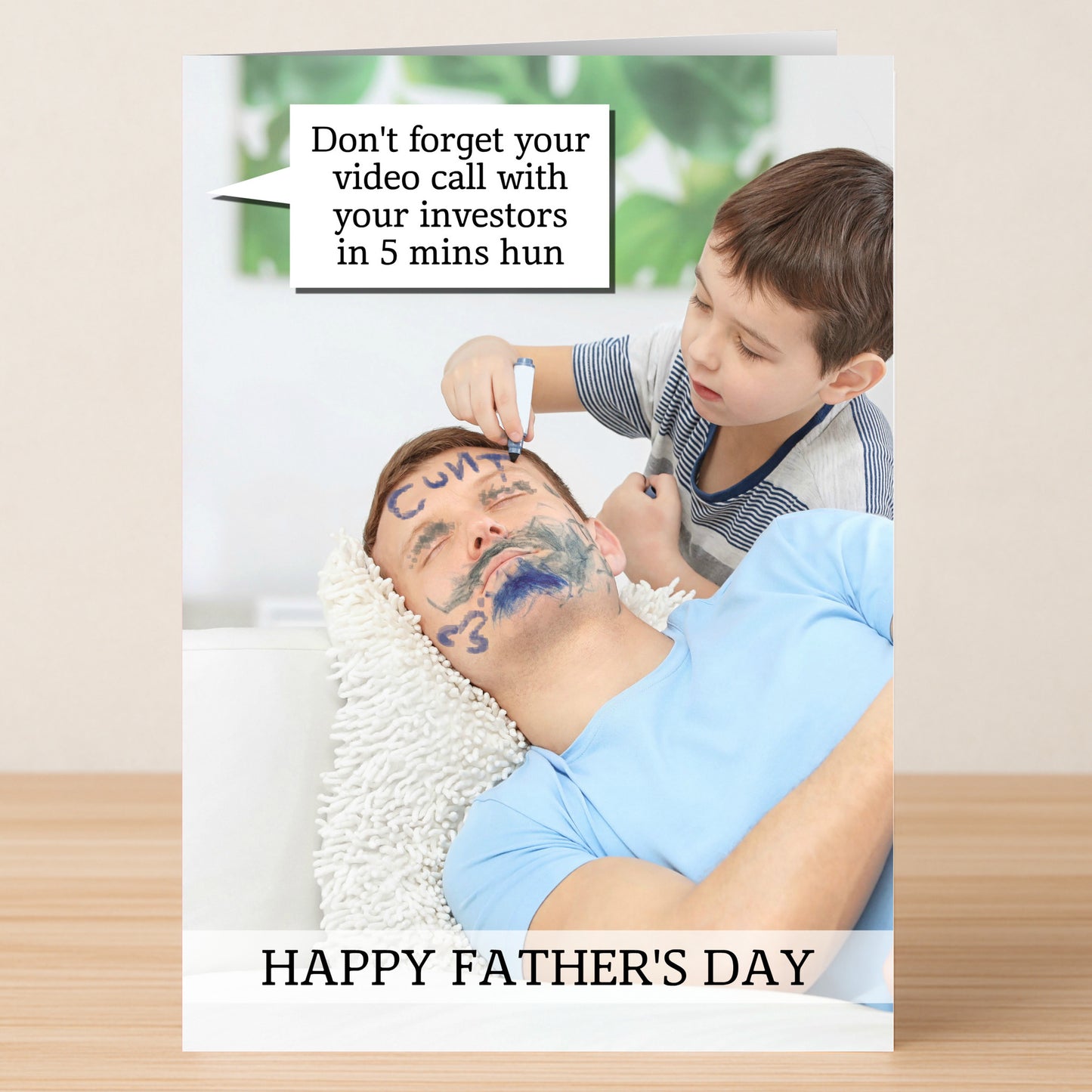 The Investors Funny Father's Day Card by Twisted Gifts shows a child drawing on a dad’s face with marker while he sleeps. A speech bubble reminds him about a video call, and "Happy Father's Day" appears at the bottom.