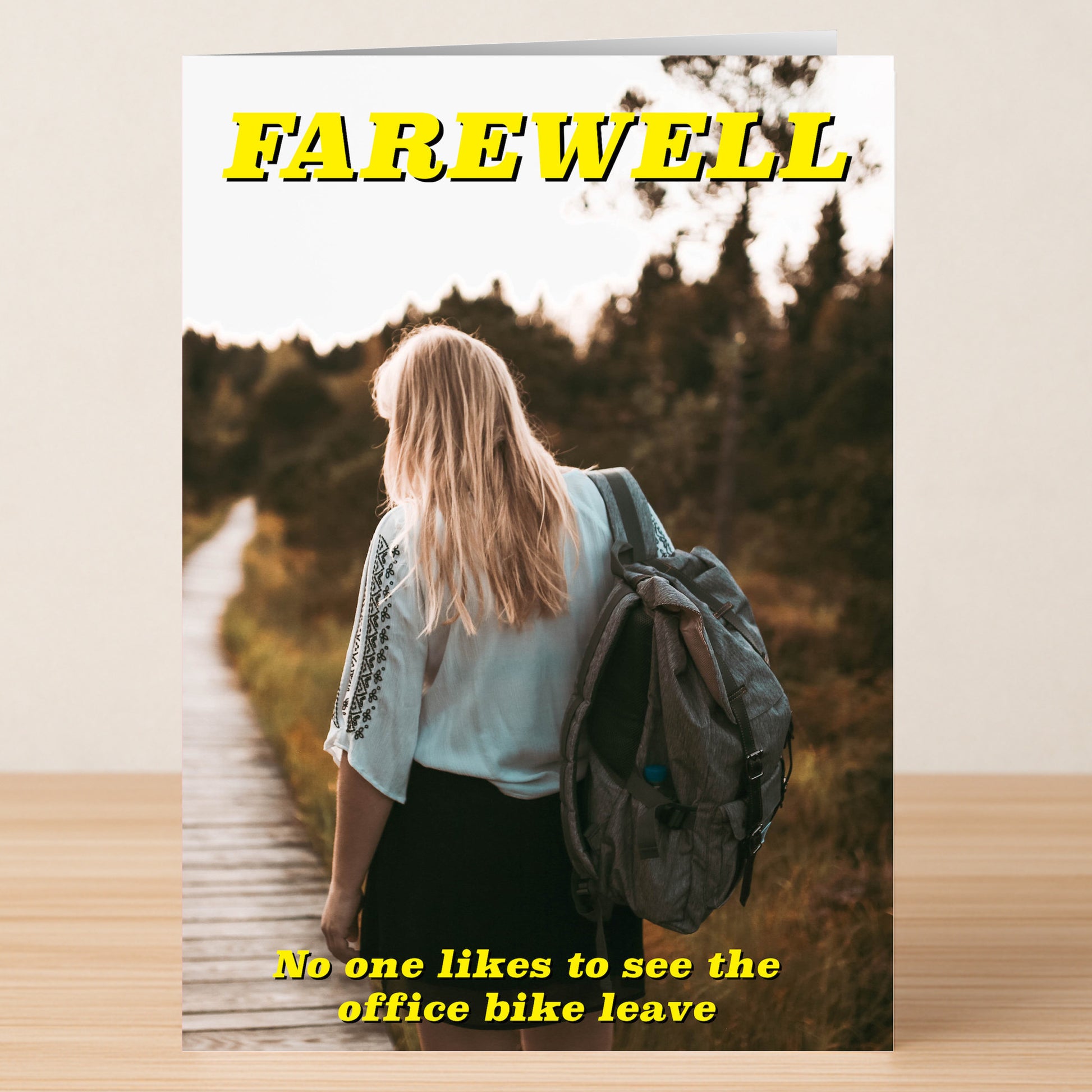 The Office Bike Insulting Farewell Card by Twisted Gifts features a figure with long blonde hair walking away on a wooden path, holding an Office Bike helmet and bag, with bold yellow farewell text.