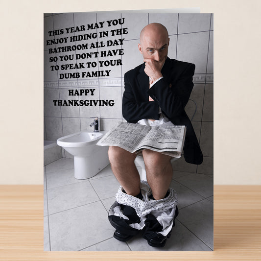 A man in a suit sits on a toilet reading a newspaper, while Twisted Gifts’ Hiding Insulting Thanksgiving Card adds holiday cheer with witty insults and a funny message about dodging family.