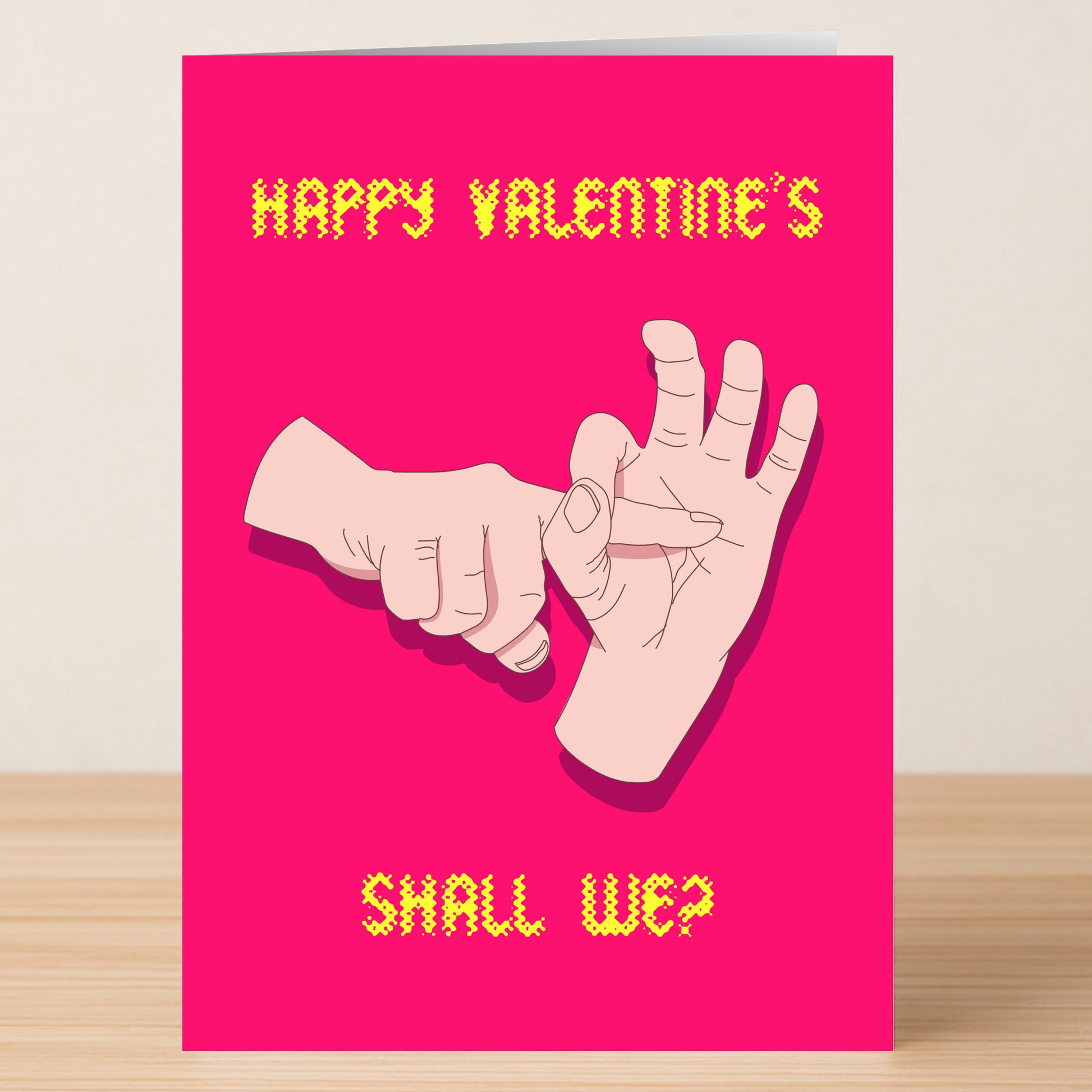 The Shall We Rude Valentine's Card by Twisted Gifts is a pink card with yellow text, "Happy Valentine's Shall We?", and a cheeky illustration of one hand making a hole and another inserting a finger.