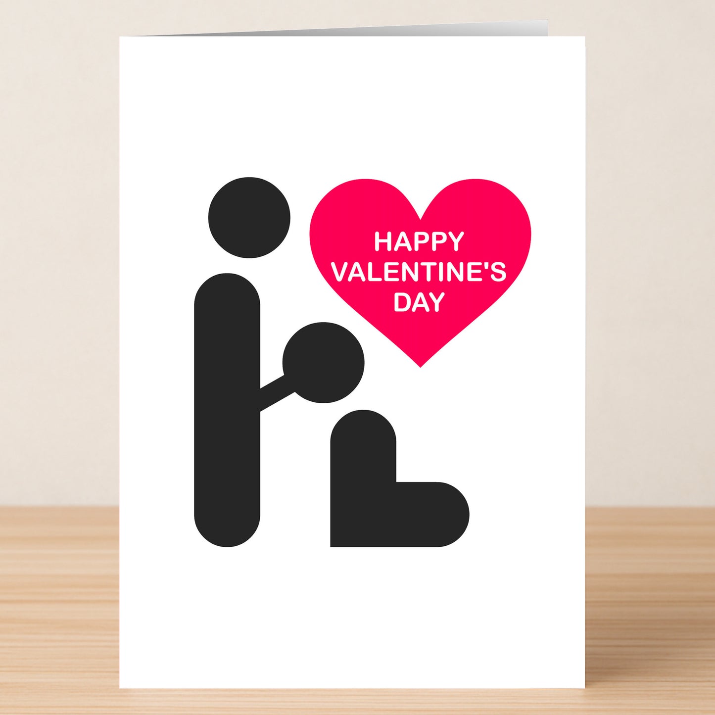 The Simple BJ Rude Valentine's Card by Twisted Gifts features minimalist figures—one kneeling before another with a pink heart above that says "HAPPY VALENTINE'S DAY." Its cheeky, humorous design pops on a wooden surface.