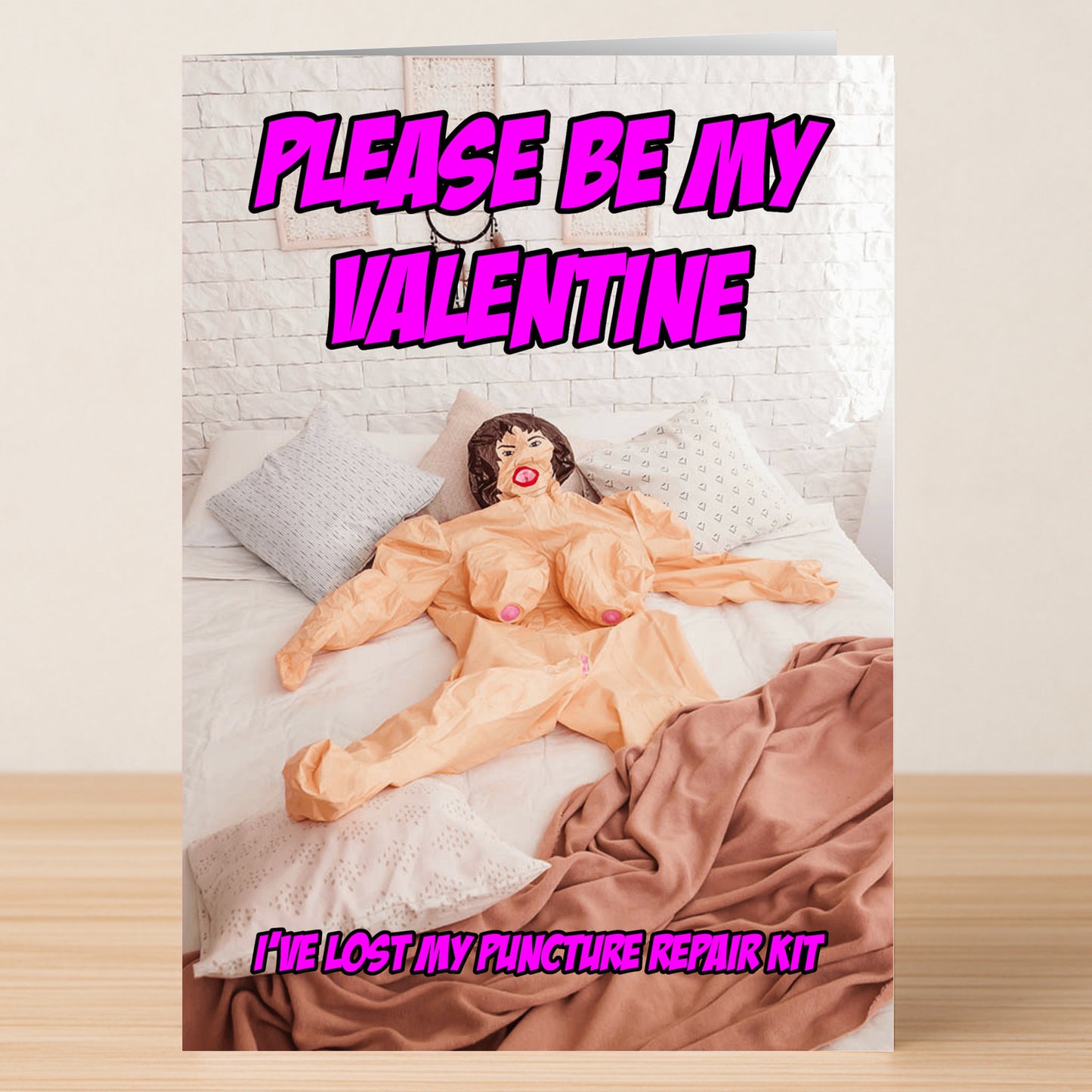 The Repair Kit Rude Valentine's Card from Twisted Gifts features a blow-up doll on a bed with pillows and blanket, plus the text "PLEASE BE MY VALENTINE. I'VE LOST MY REPAIR KIT." It's the perfect sarcastic card for Valentine's Day!.