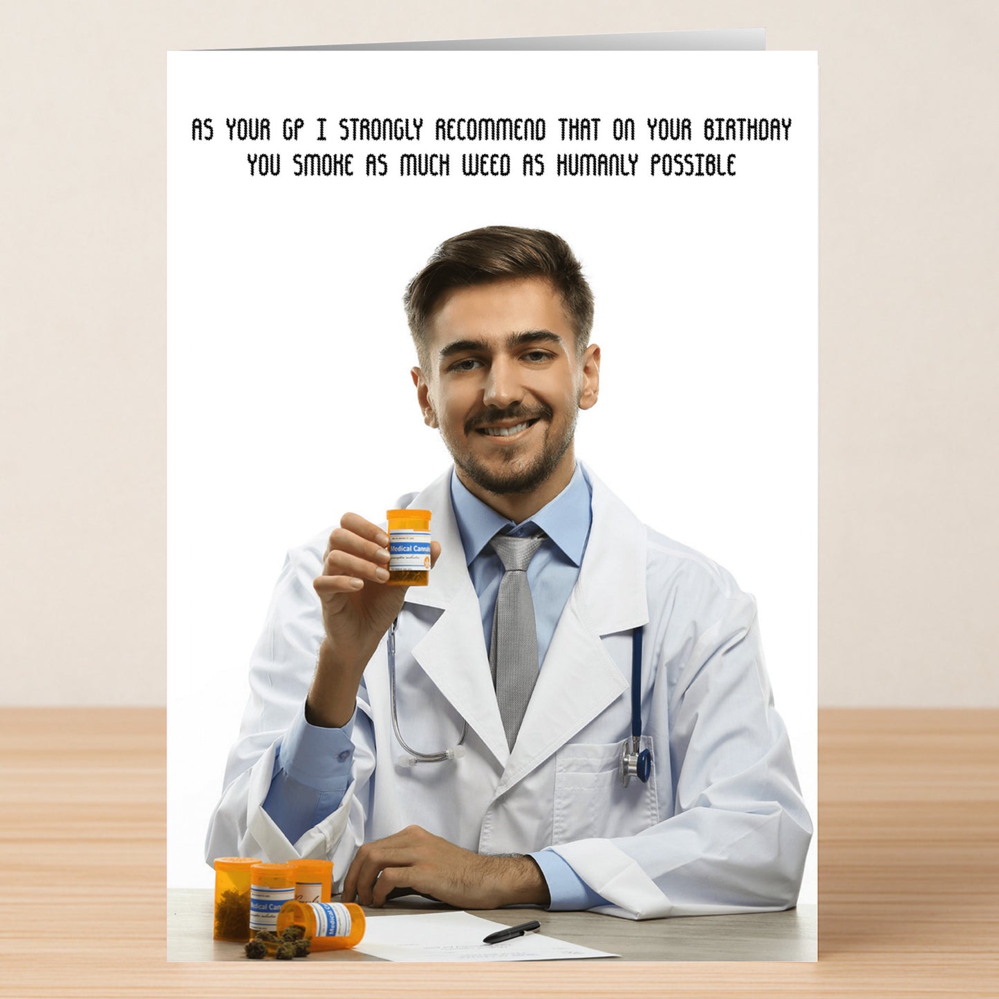 A smiling male doctor in a white coat holds a prescription bottle, with text above: "As your GP I strongly recommend that on your birthday you smoke as much weed as humanly possible." Humanly – Funny Birthday Card by Twisted Gifts. Perfect for friends who love a laugh!.