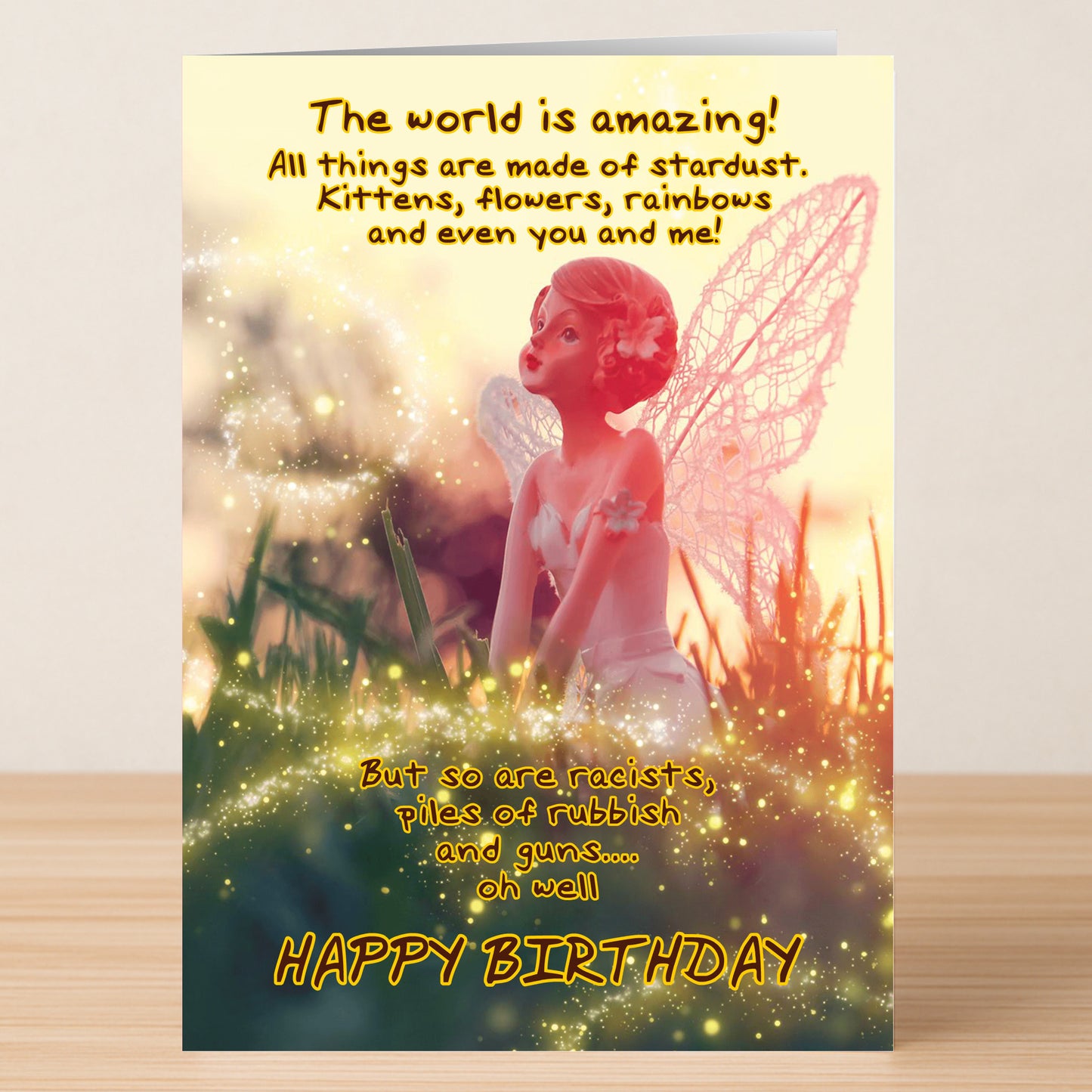 The Star Dust – Funny Birthday Card by Twisted Gifts features a fairy figurine amid glowing lights and whimsical text about the world’s wonders and flaws, ending with "HAPPY BIRTHDAY.