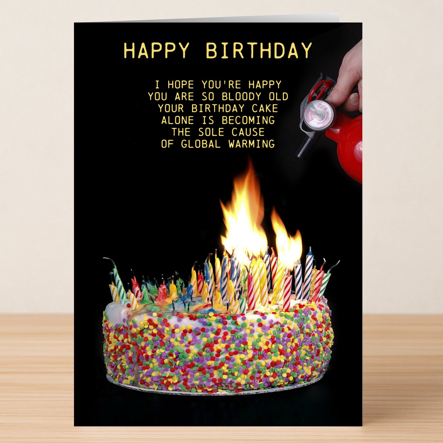 The Twisted Gifts Candles – Insulting Birthday Card features a cake ablaze with candles and a hand reaching for a fire extinguisher, with a joke about global warming—ideal for anyone who enjoys cheeky birthday humor!.