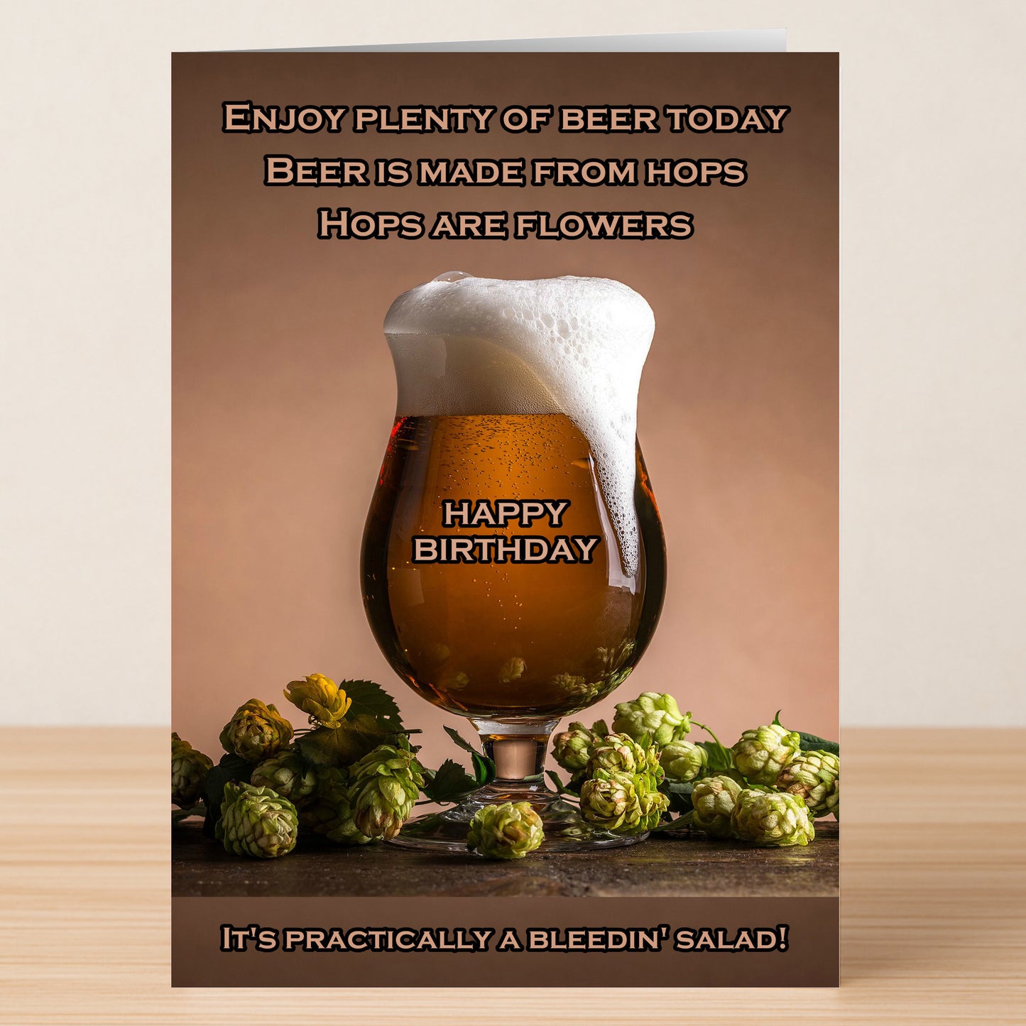 A tulip glass of beer with a foamy head sits among fresh hops; the "Salad – Funny Birthday Card" by Twisted Gifts features humorous wishes comparing beer to a salad.