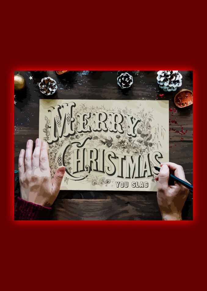 A hand holding a Twisted Gifts You Slag Rude Christmas Card in front of a red background.