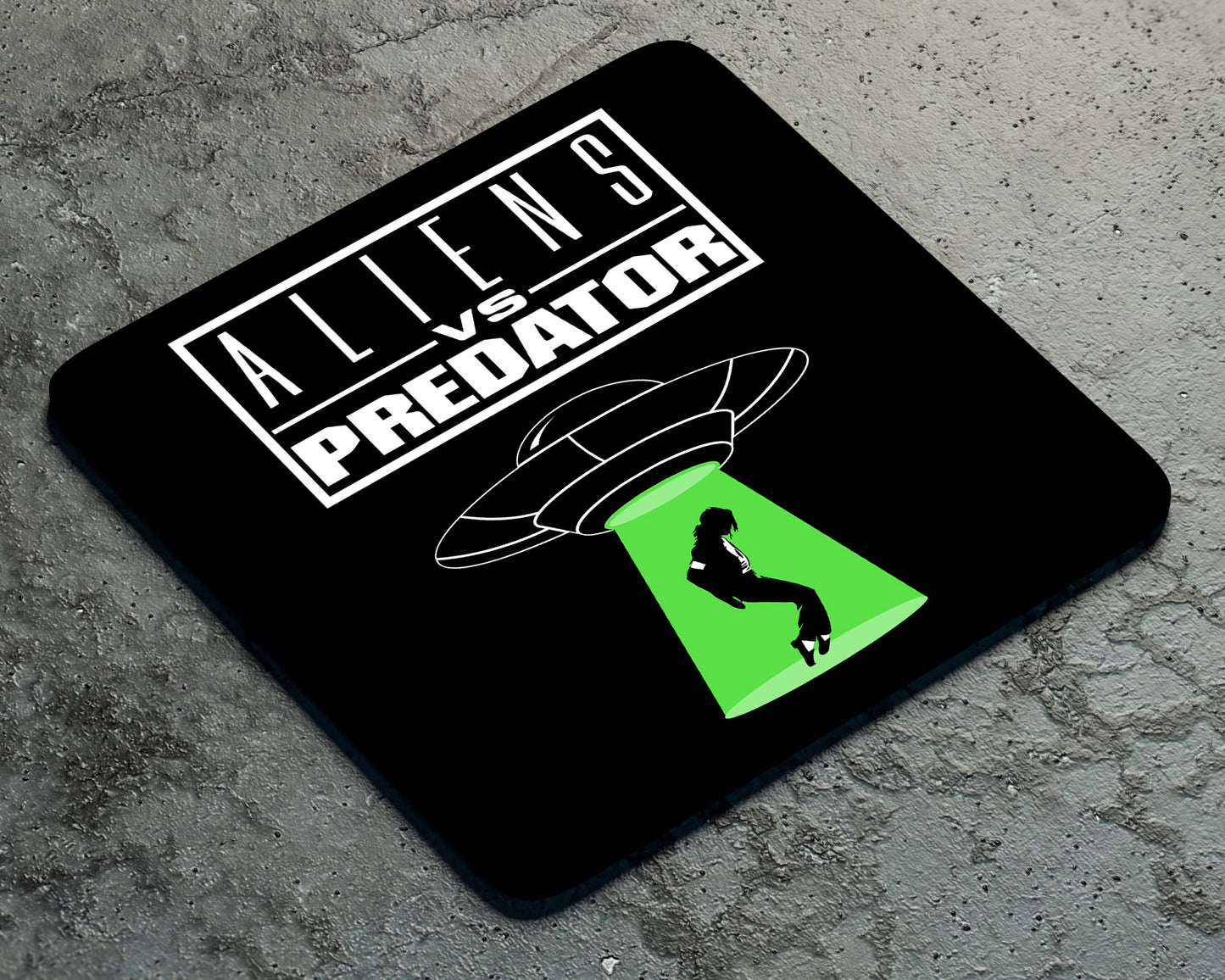 The Twisted Gifts Aliens Vs Preditor Coaster features black design, "Aliens vs Predator" text, and a graphic of a person abducted by a UFO—a great pop culture gift or quirky addition to any desk.
