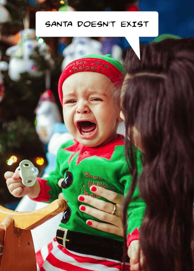 A baby crying in front of a Christmas tree with a speech bubble saying Santa doesn't exist, creating an Exist Funny Christmas Card from Twisted Gifts.